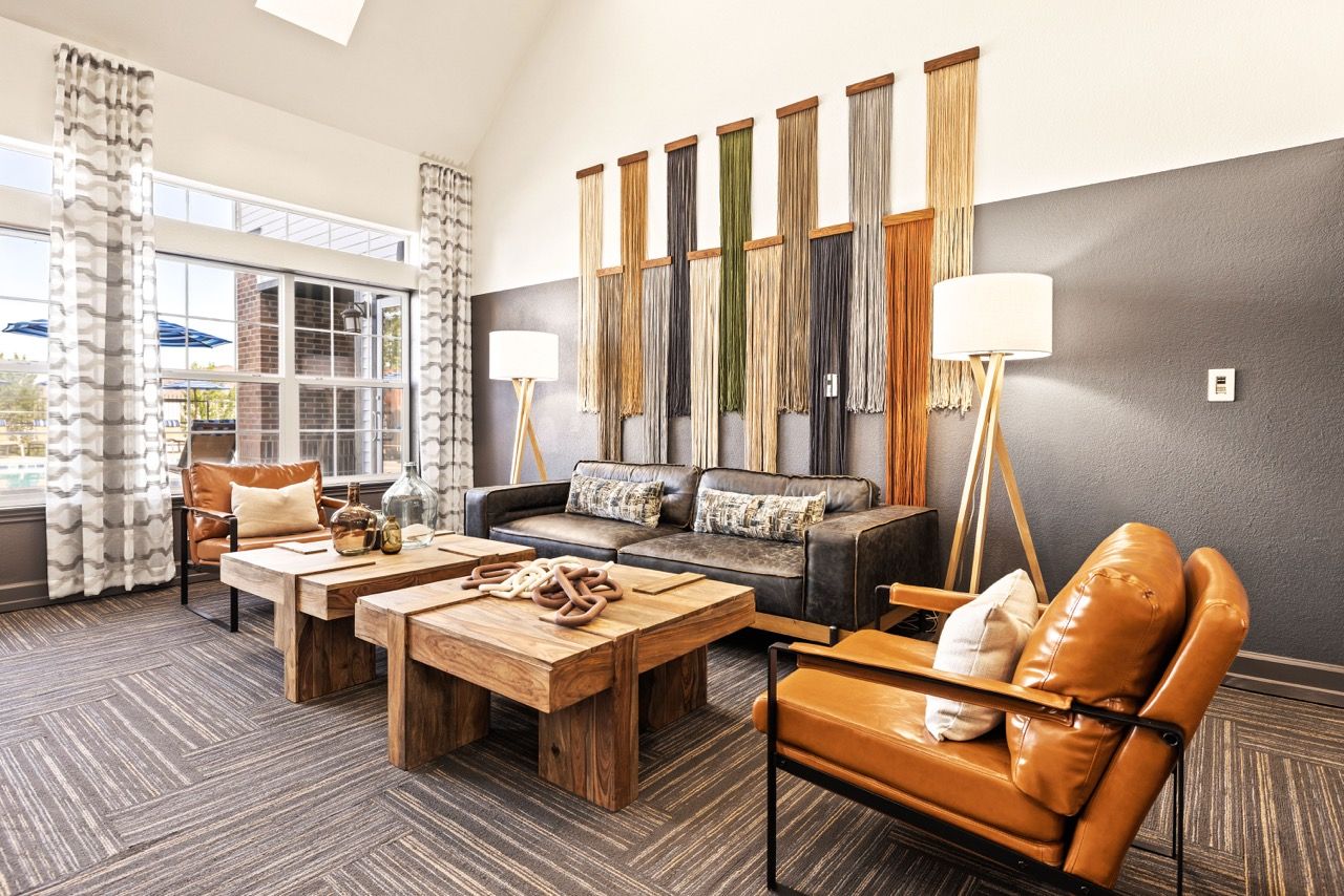 Contemporary apartment community lounge with leather seating, wooden coffee tables, and large windows at The Preserve at Greenway Park.