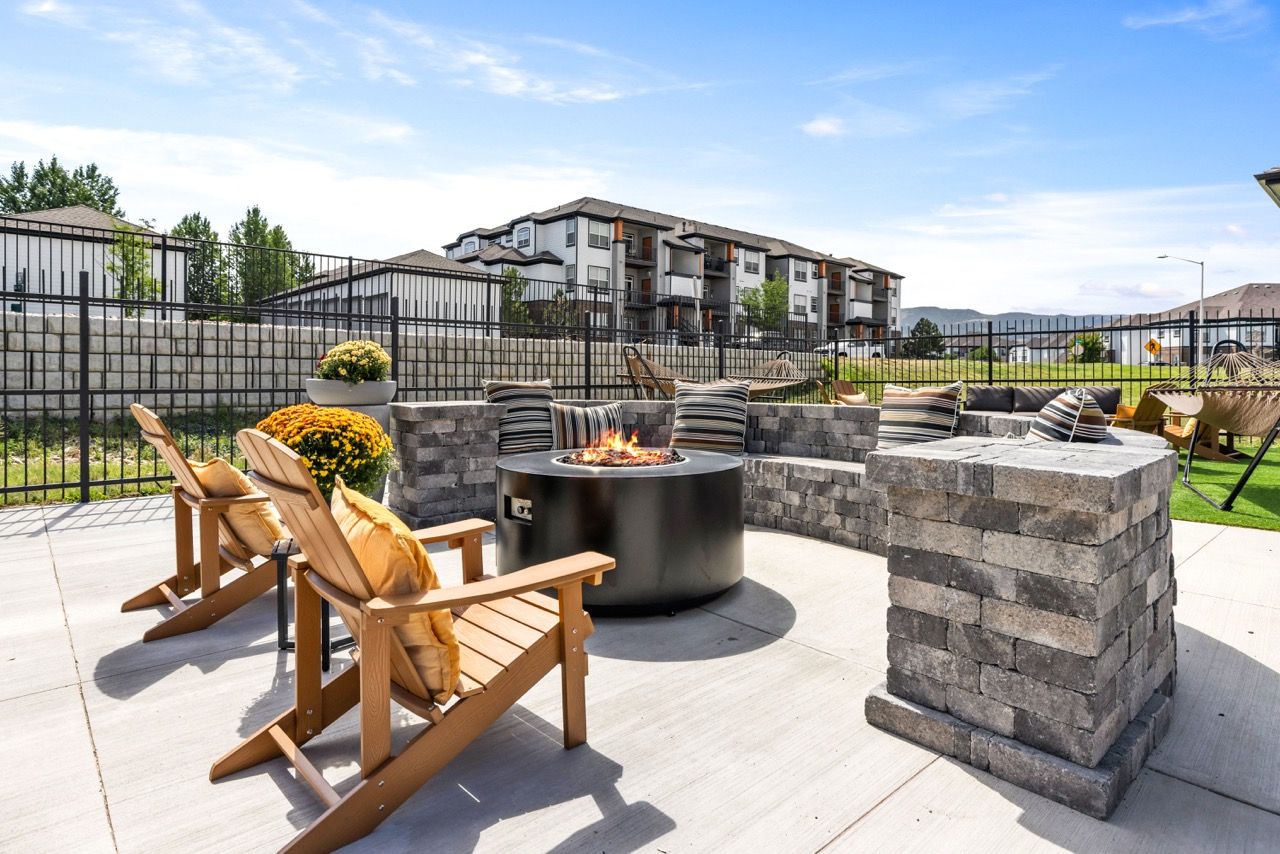 Outdoor communal patio with a circular fire pit, cushioned lounge chairs, and stacked stone seating at The Preserve at Greenway Park.