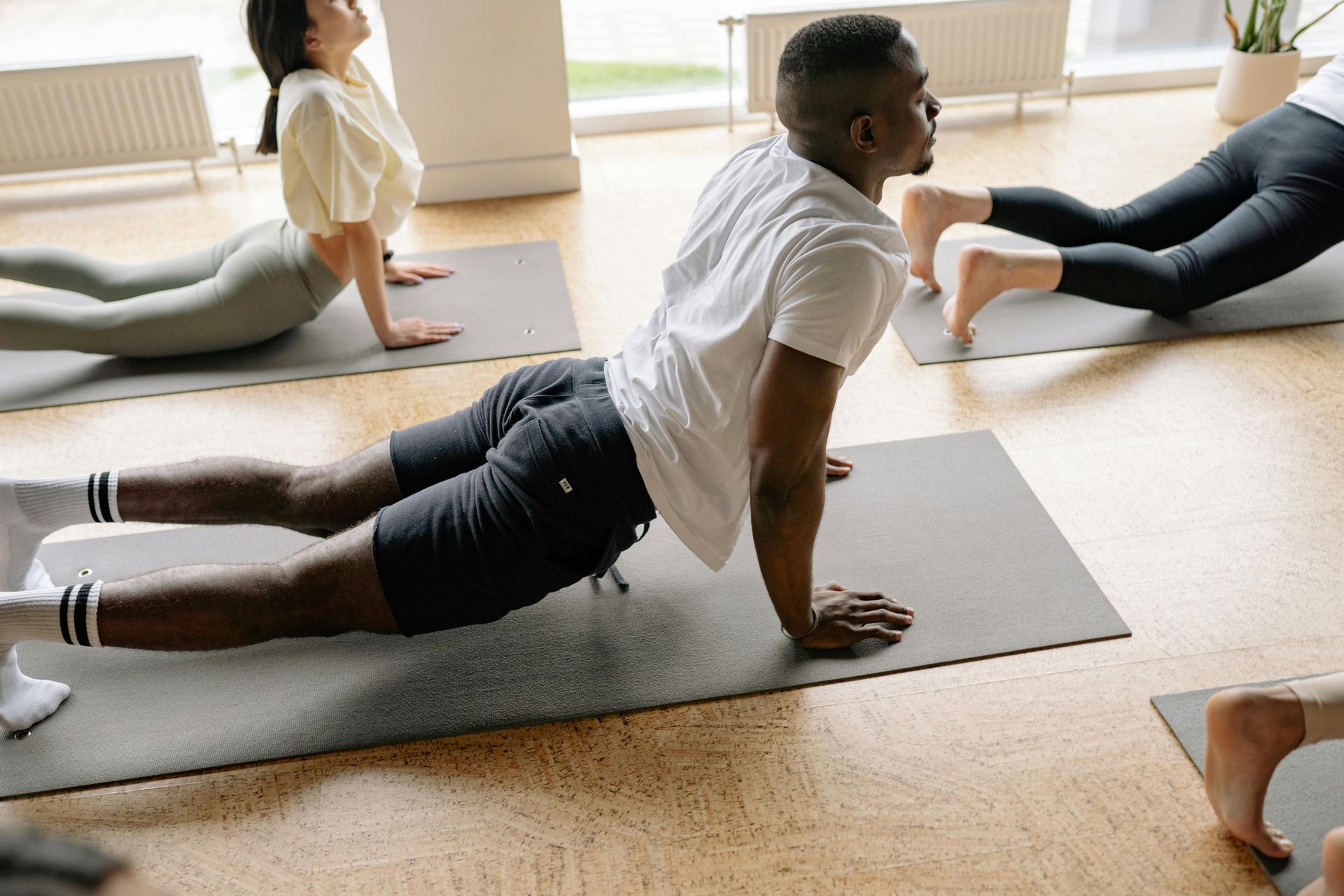 A group of people performing the upward-facing dog yoga pose on mats in a bright, indoor studio.