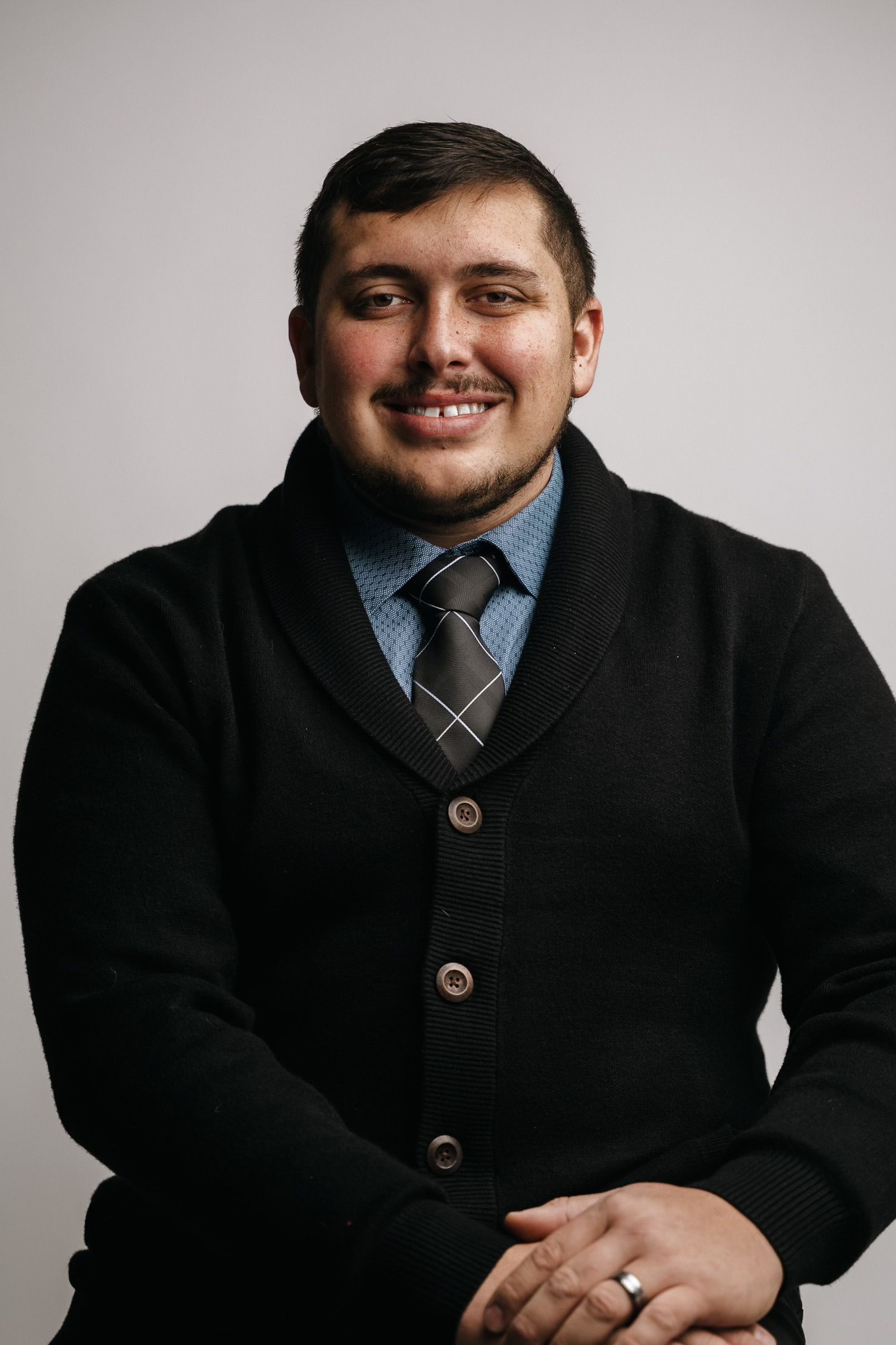 A man wearing a black sweater and tie is smiling for the camera.