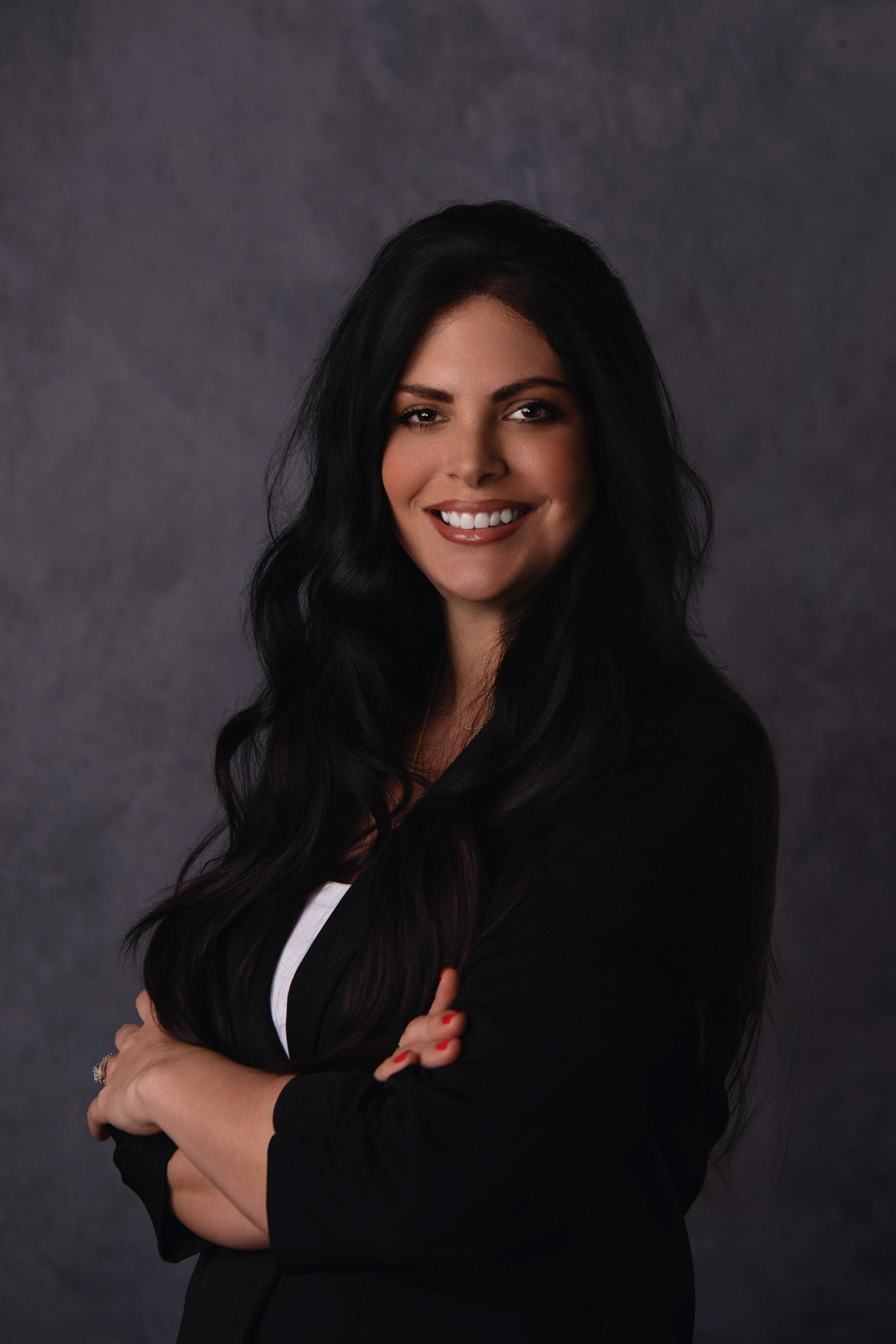 A woman with long black hair is posing for a picture with her arms crossed.