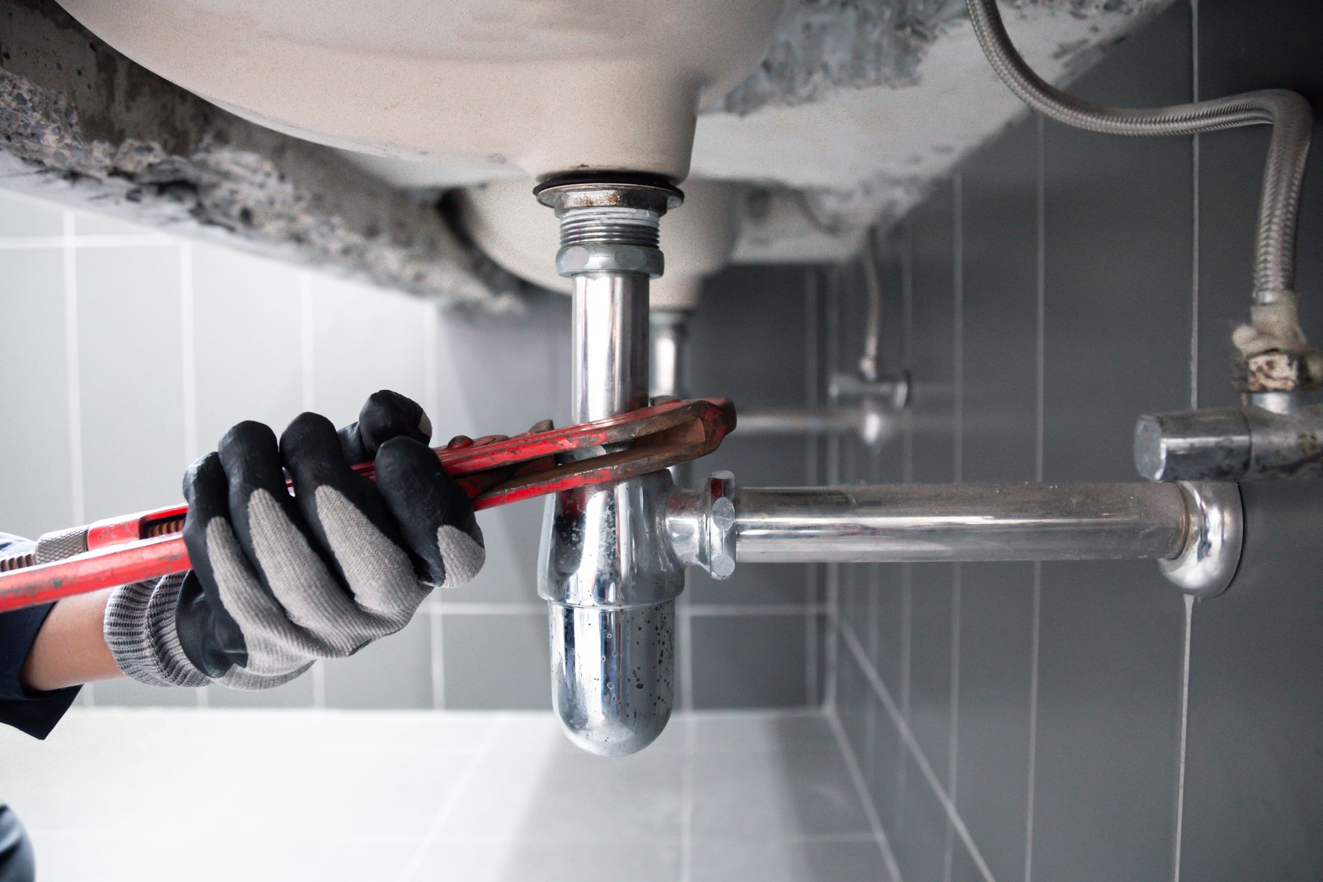 Worker tightening a sink pipe with a wrench under a bathroom basin.