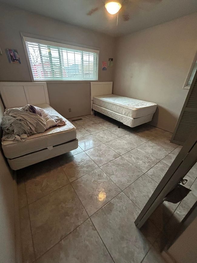 Spare bedroom with two twin beds, tiled floor, and window blinds.