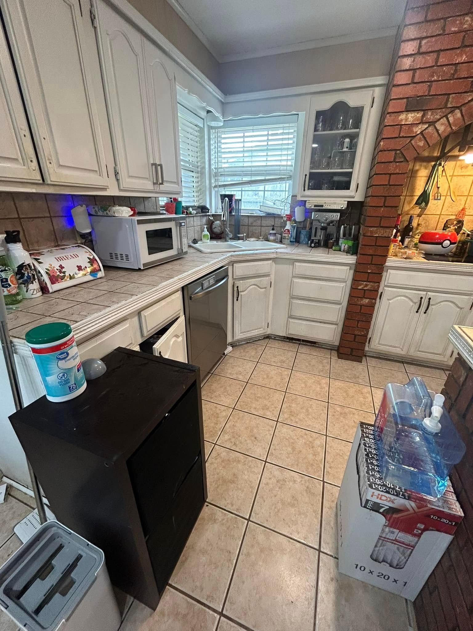 Small kitchen with white cabinets, black mini fridge, tiled floor, and sink by a window.