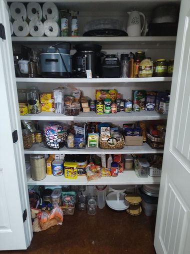 Open pantry shelves packed with assorted canned goods, boxes, jars, and kitchen appliances.