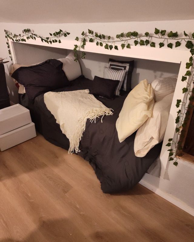 Cozy loft nook bed with dark bedding, cream pillows, a throw blanket, and faux ivy garland along the wall.