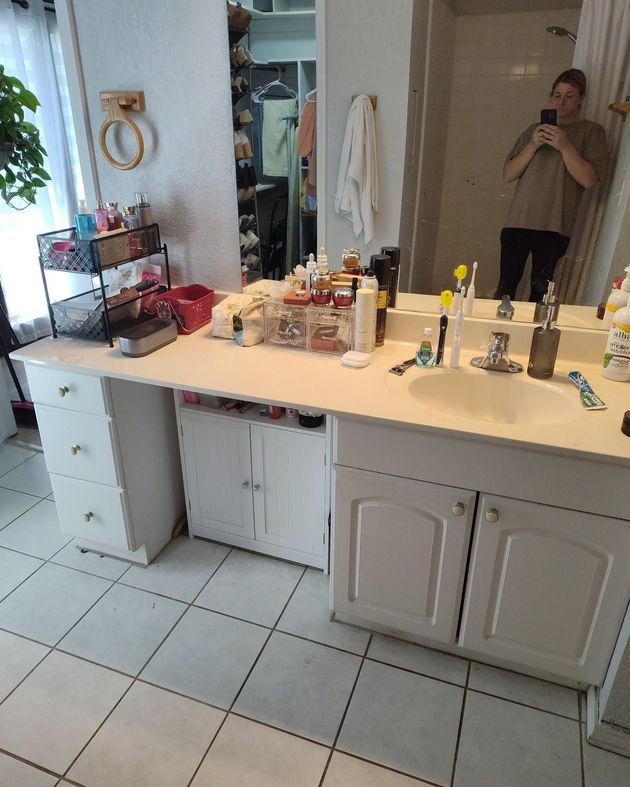 Bathroom vanity with mirror, toiletries, and a person taking a mirror selfie