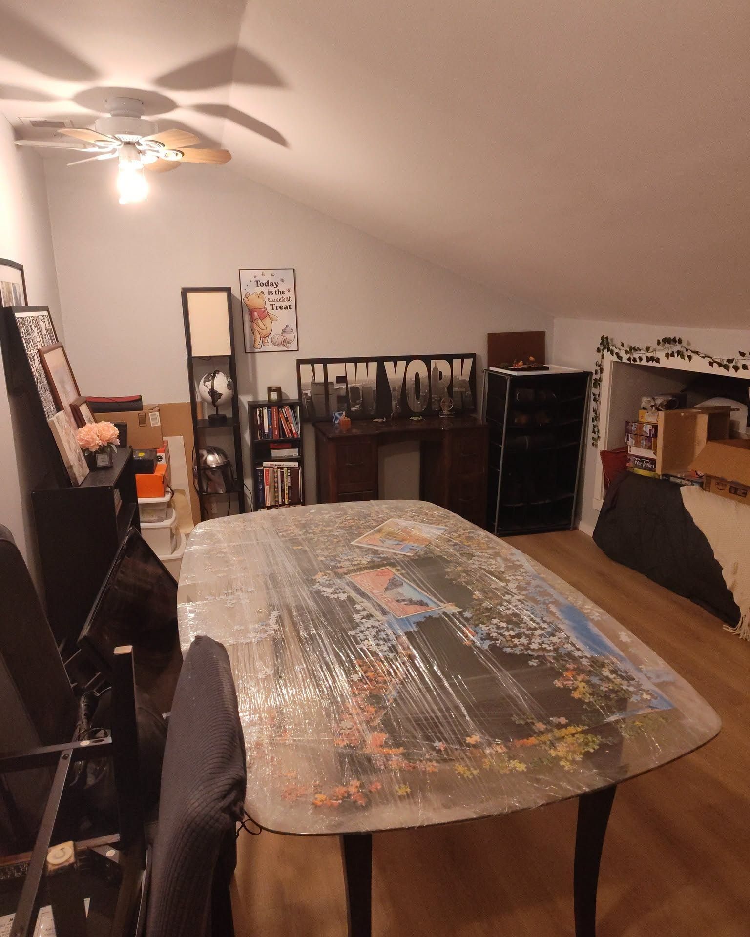 Attic bedroom with a bed covered in a puzzle mat, wooden floor, dresser, fan, and mirror.