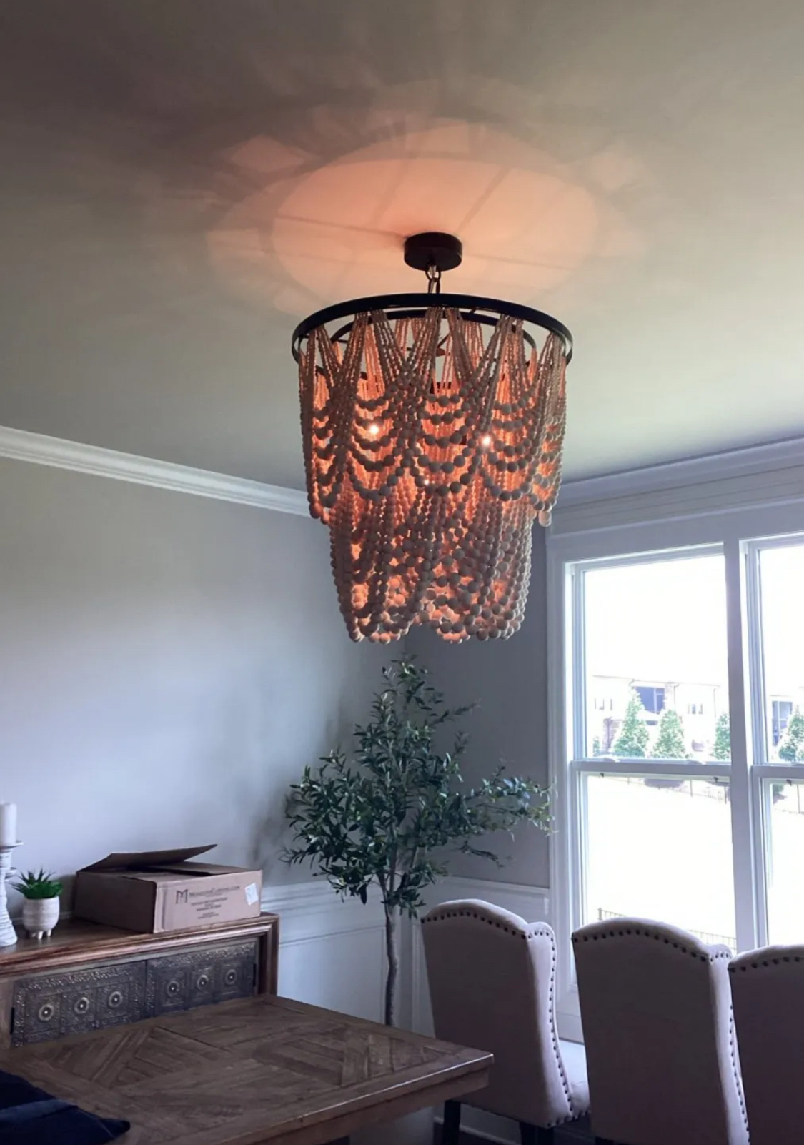 Two-tiered beige beaded chandelier hanging in a dining room with a tree.