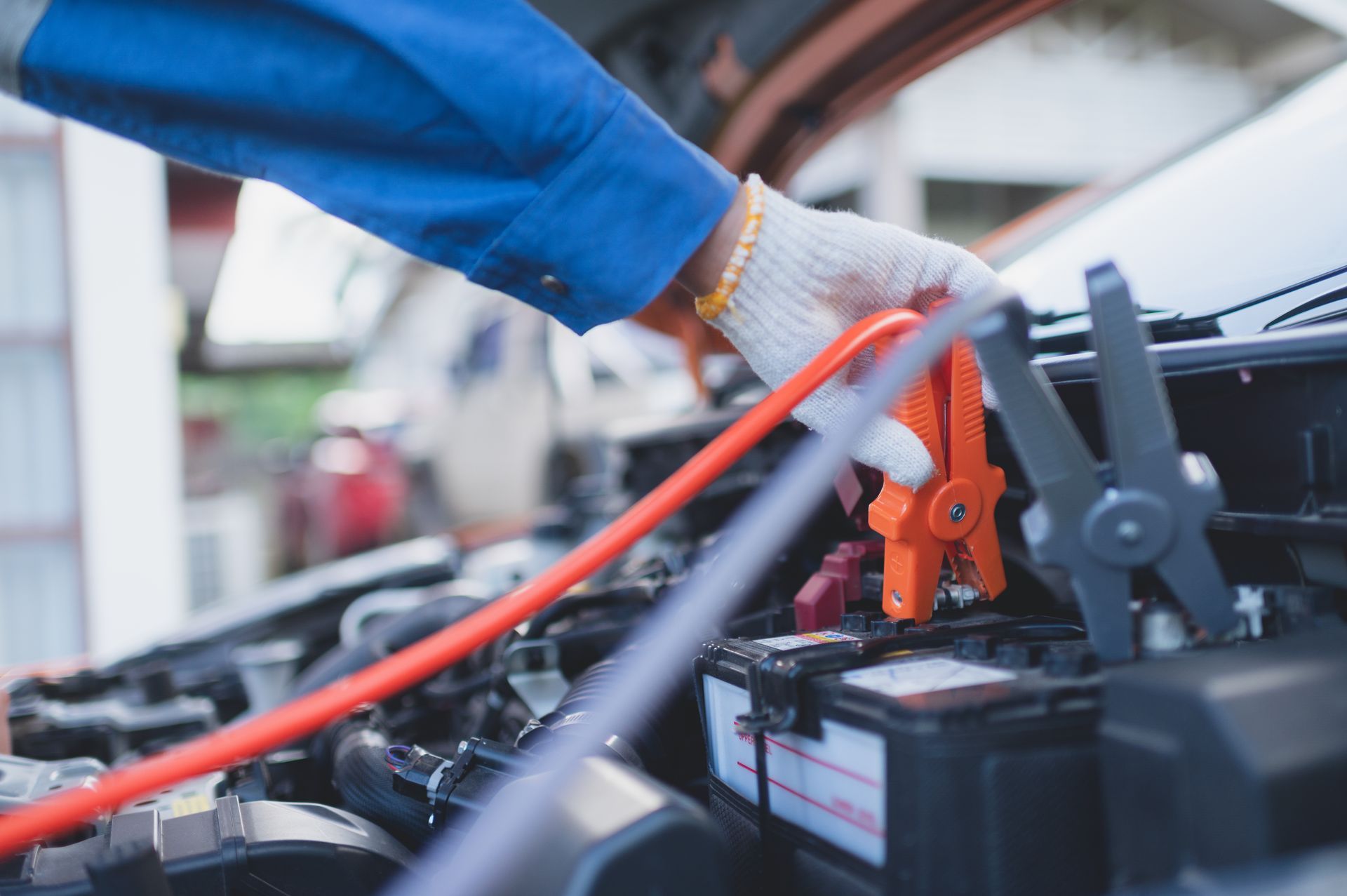 An auto electrical professional holds an orange wire, connecting it to a car engine An auto electrical professional holds an orange wire, connecting it to a car engine