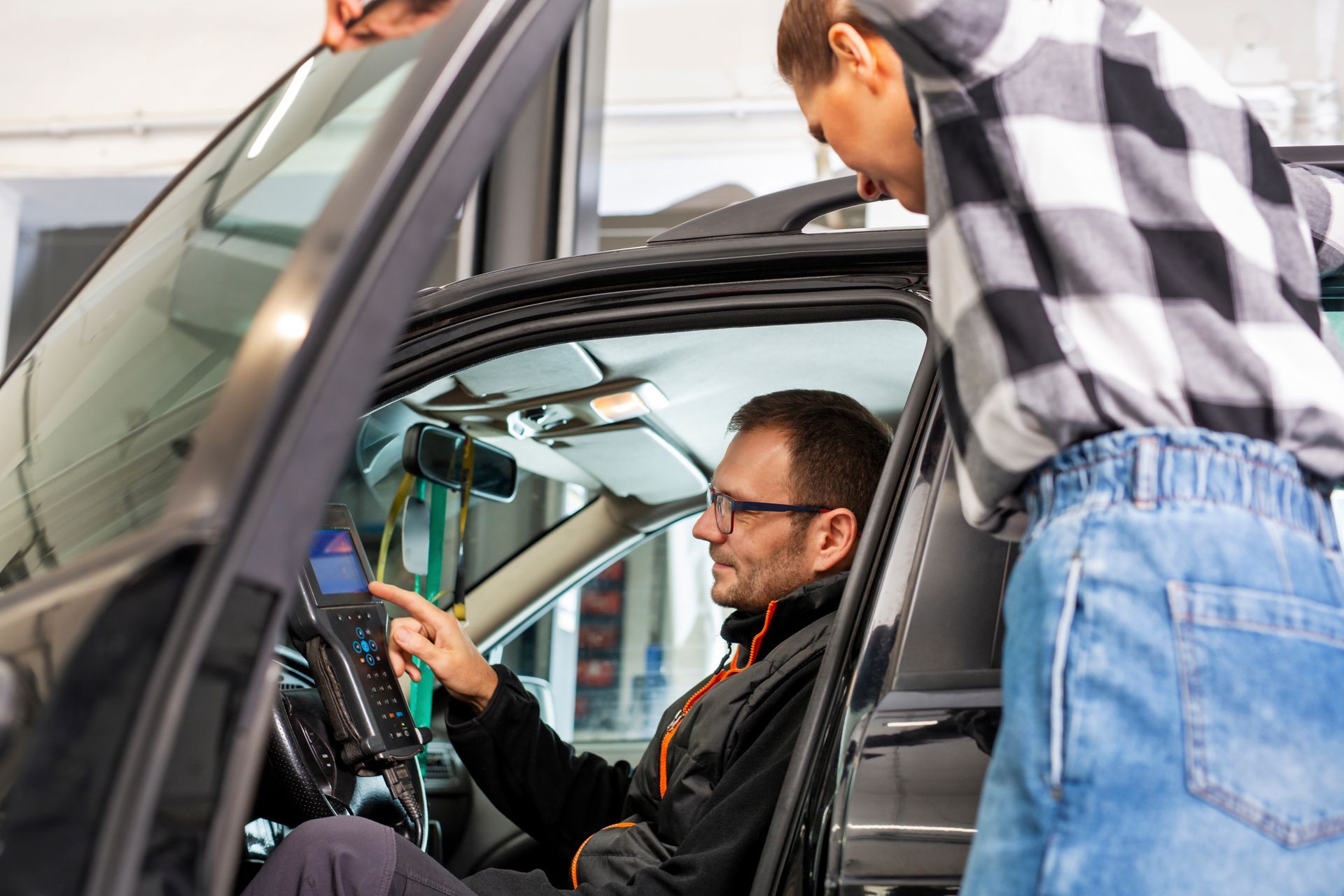 A car electrician inside a car is showing an odometer to a client.