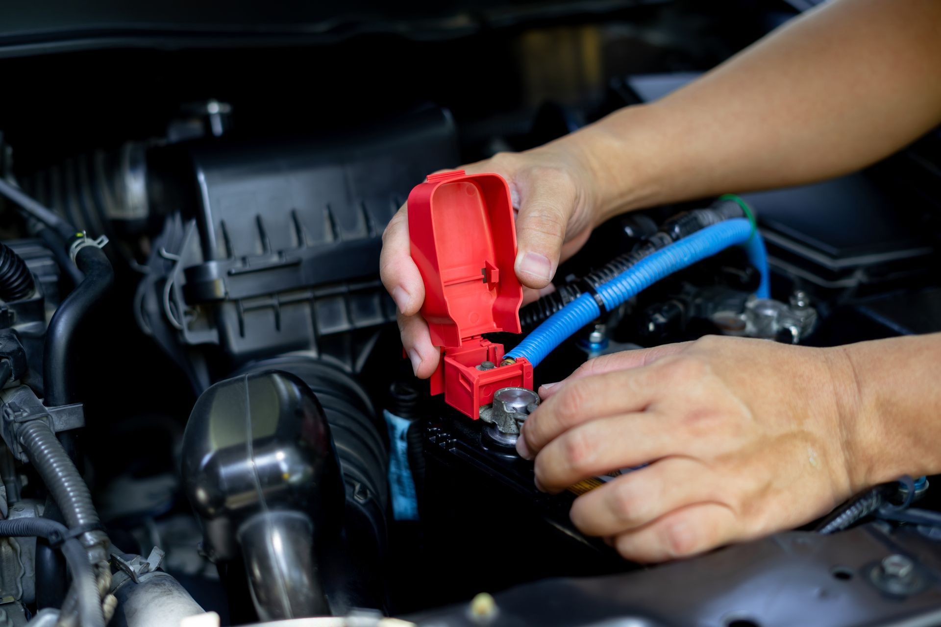 An auto electrician using a red tool to open a car battery compartment on a device An auto electrician using a red tool to open a car battery compartment on a device