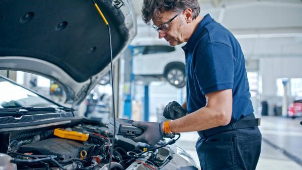 A mechanic is operating a diagnostic device connected to a car engine in an auto repair shop.