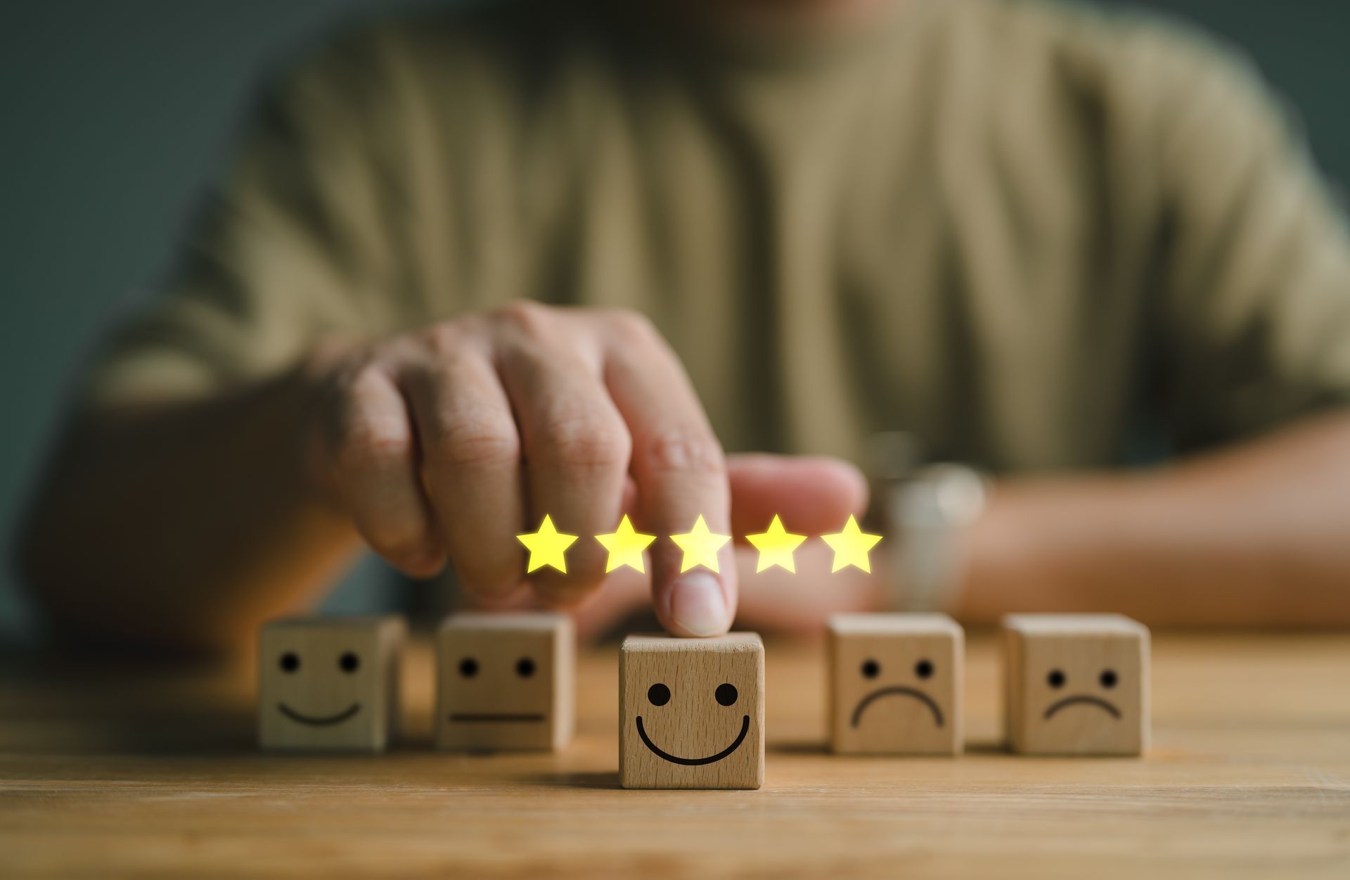 Person placing a glowing five-star rating on a happy face block, with other blocks showing different emotions.