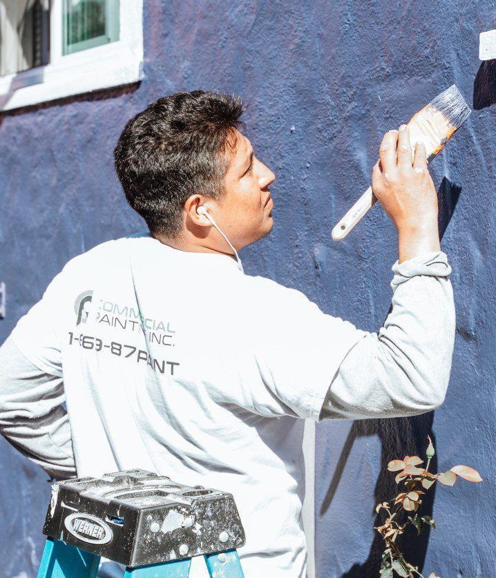 A man is standing on a ladder painting a building.