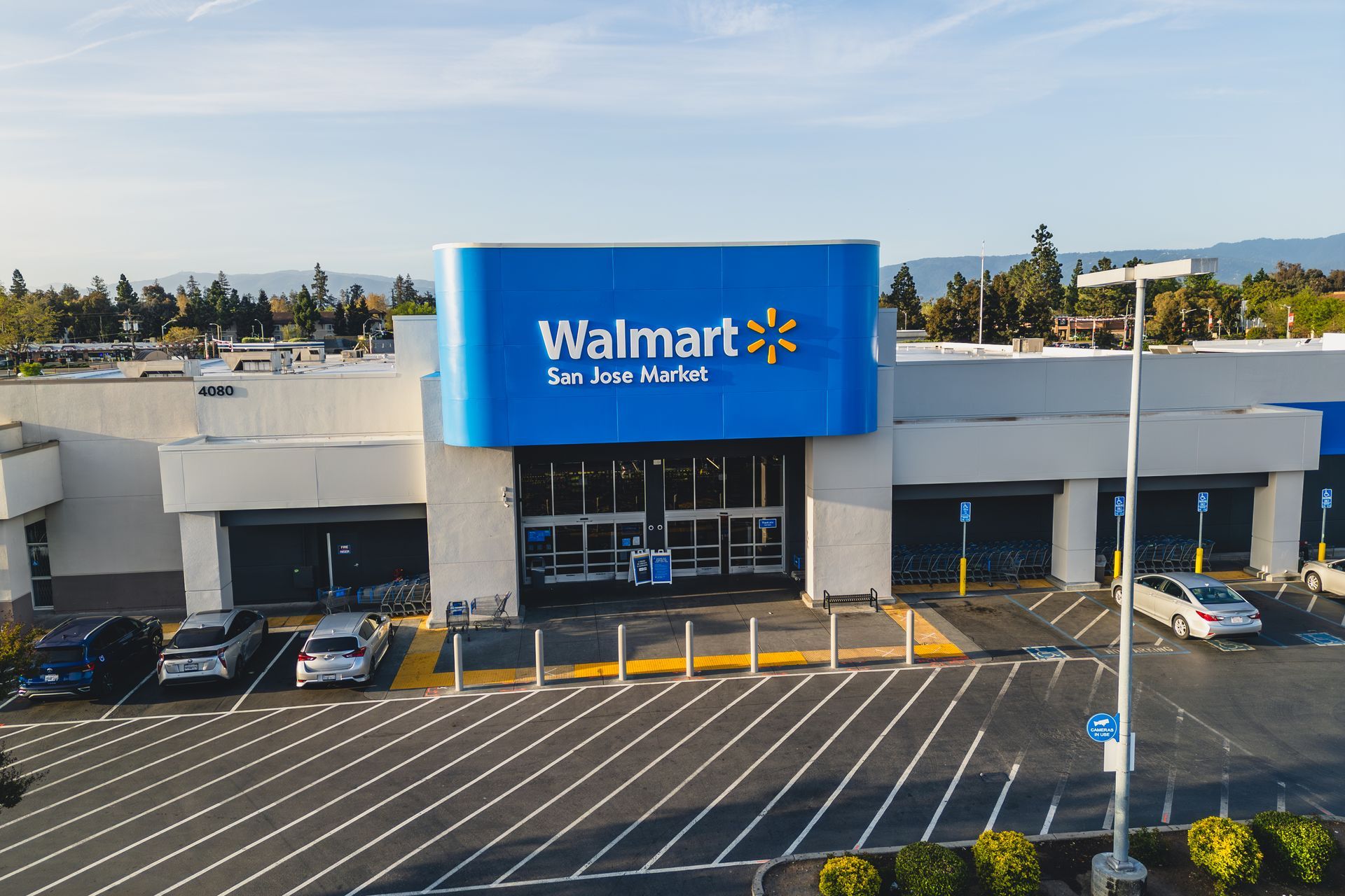 Walmart store exterior with blue signage, cars in the parking lot, and a sunny day.