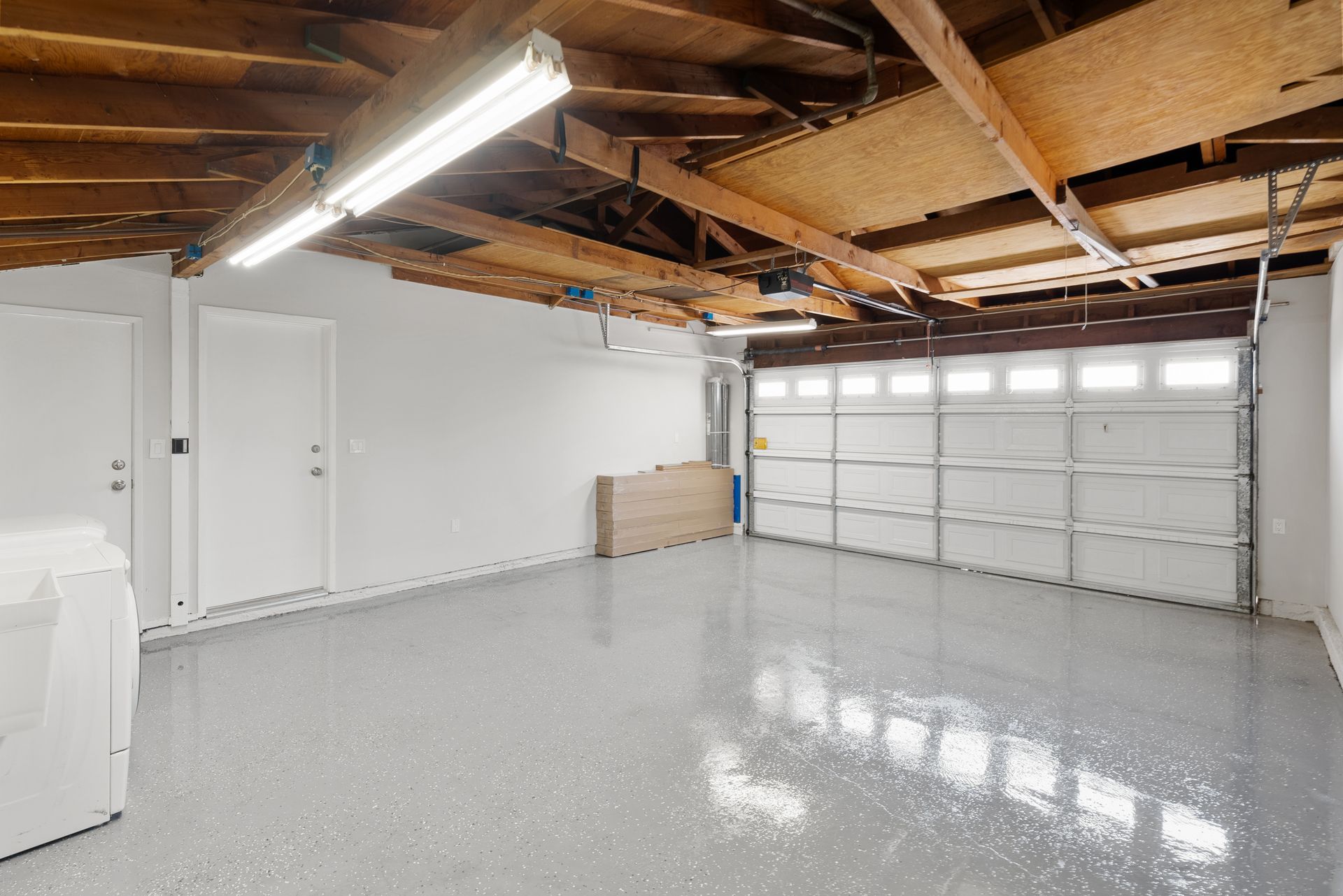 Empty garage with a glossy gray floor, white walls, and open garage door.