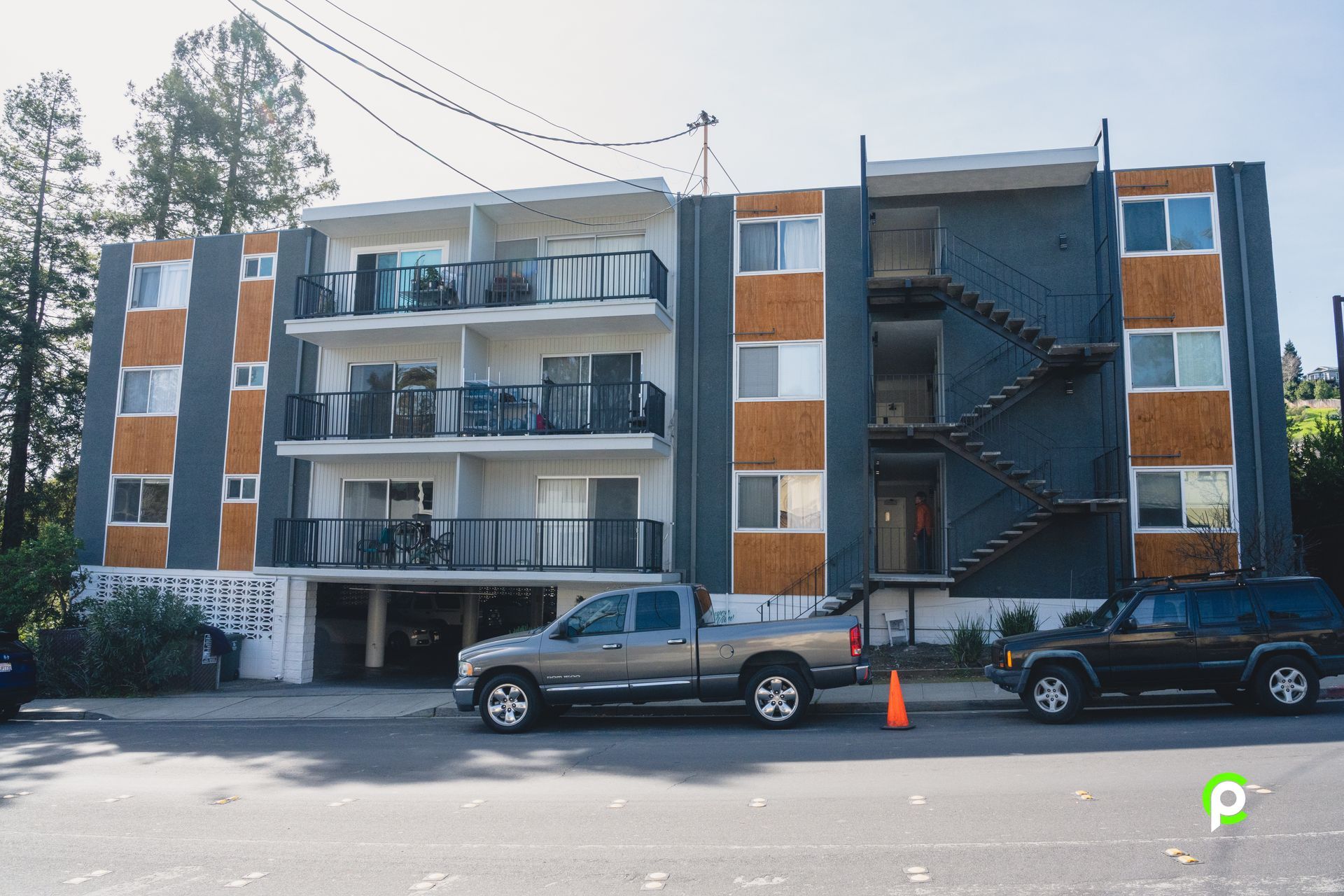 Two cars are parked in front of a large apartment building