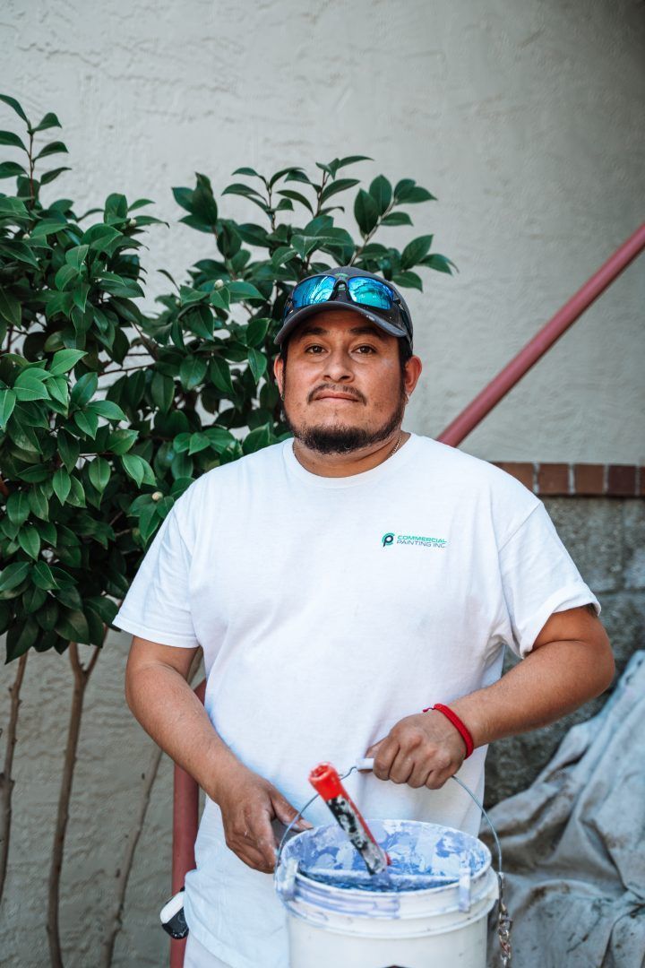 A man in a white shirt is holding a bucket of paint.