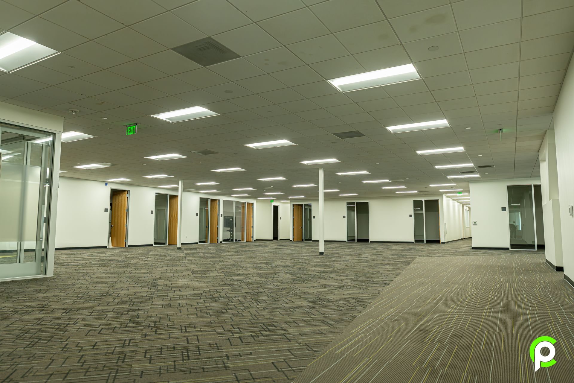 A large empty room with a green exit sign on the ceiling