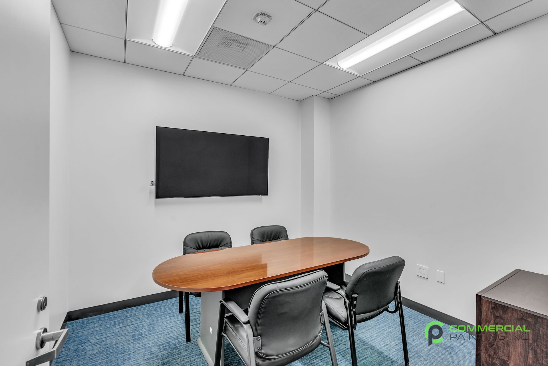 A conference room with a table and chairs and a flat screen tv on the wall.