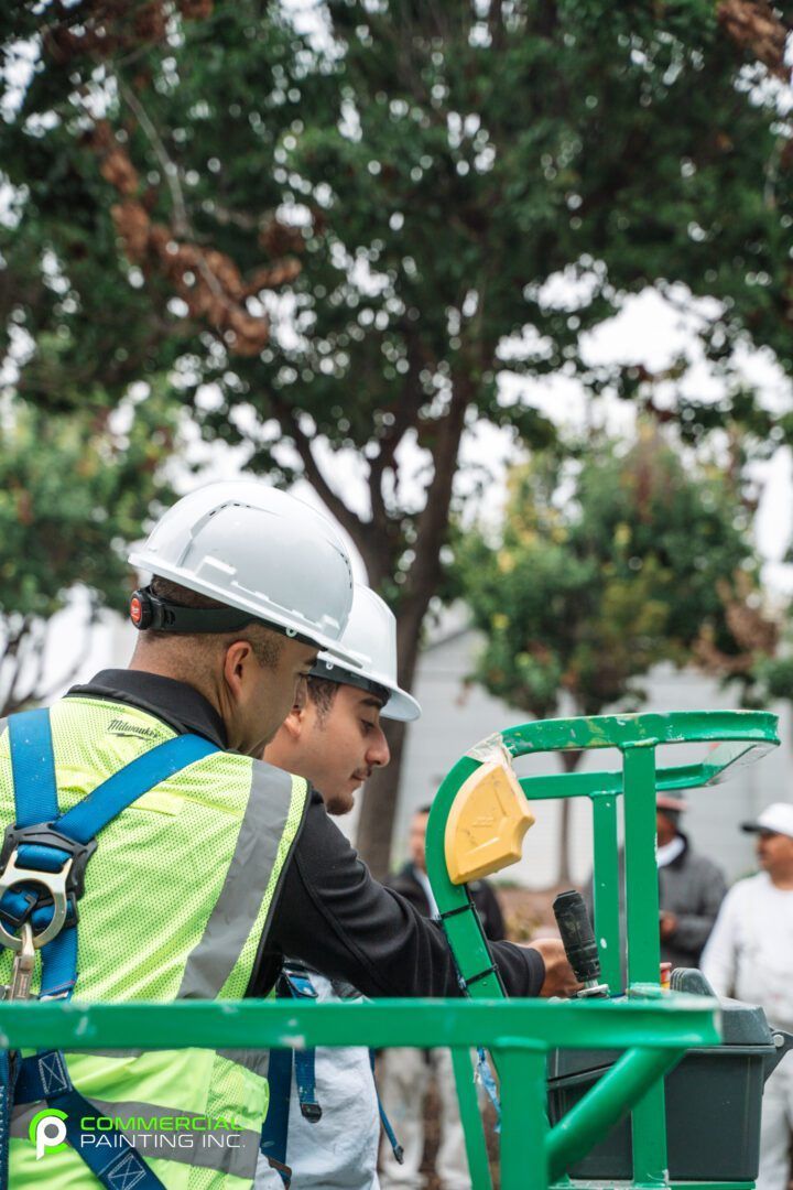 A man wearing a hard hat and safety vest is working on a green machine.
