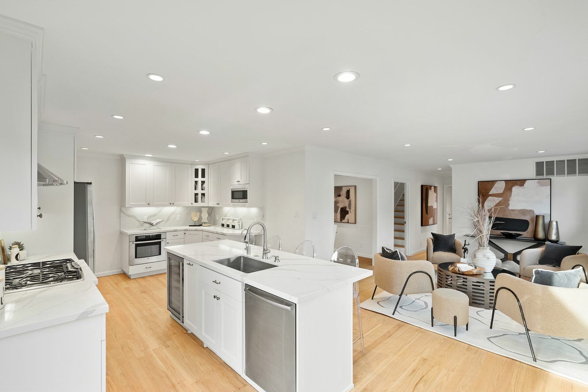 A kitchen with white cabinets and stainless steel appliances is open to a living room and dining room.