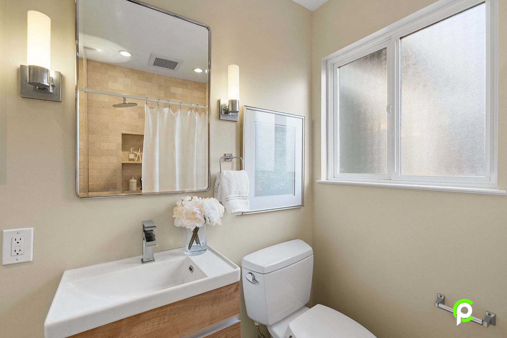 A bathroom with a toilet , sink , mirror and window.