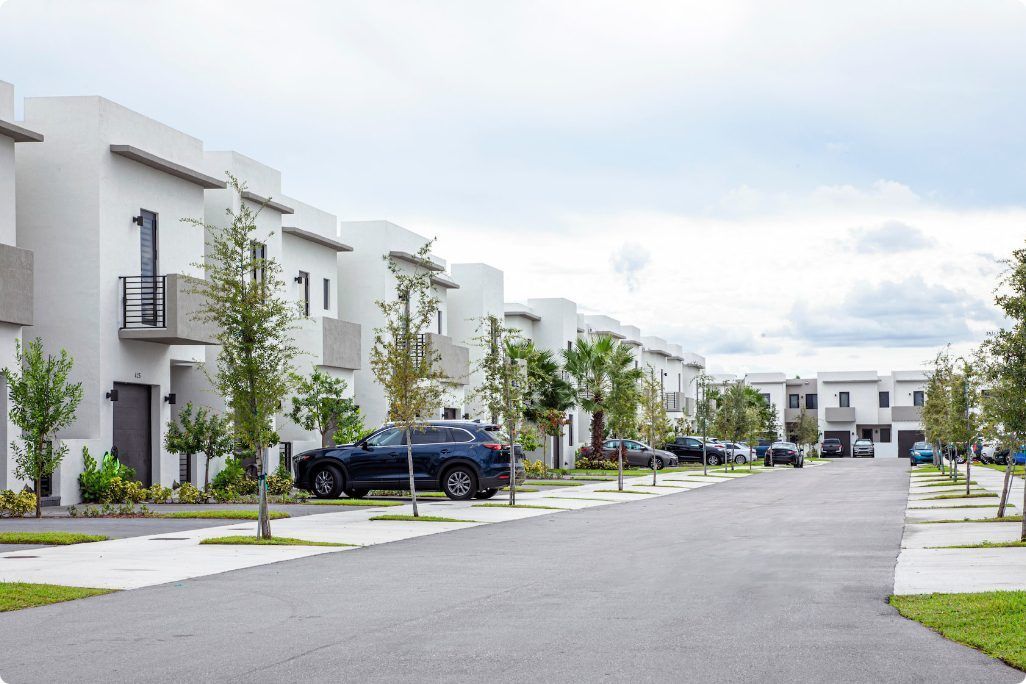 A row of white houses with cars parked on the side of the road.