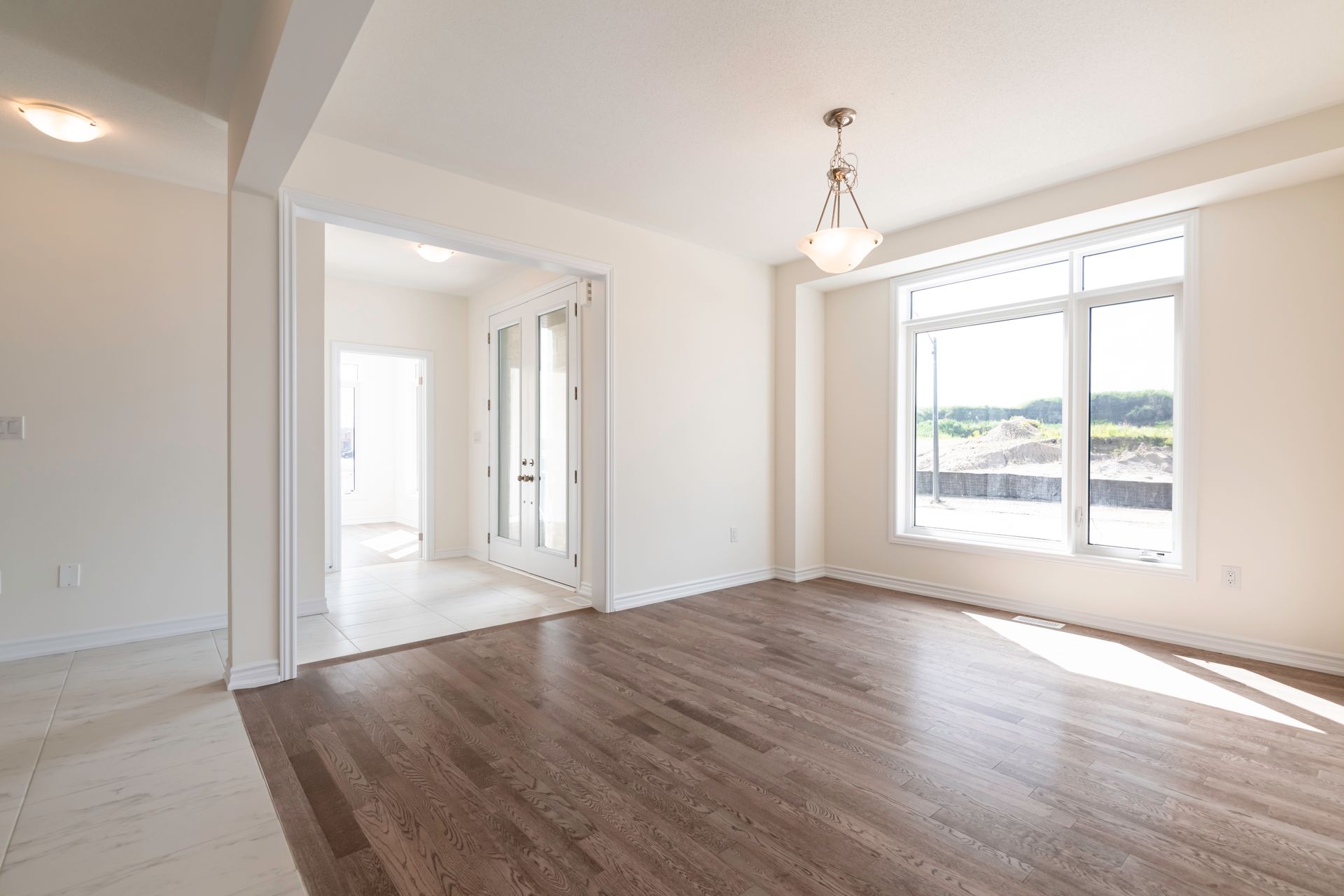 An empty living room with hardwood floors and a chandelier.