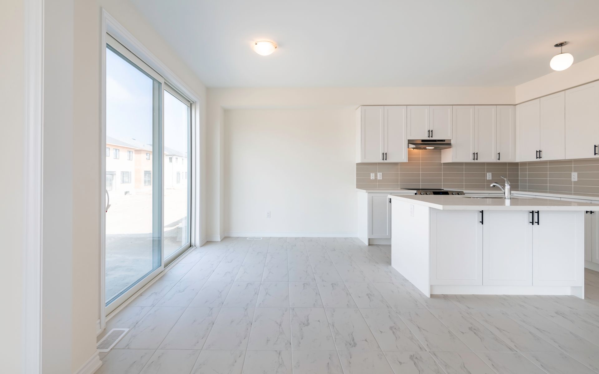 An empty kitchen with white cabinets and sliding glass doors.