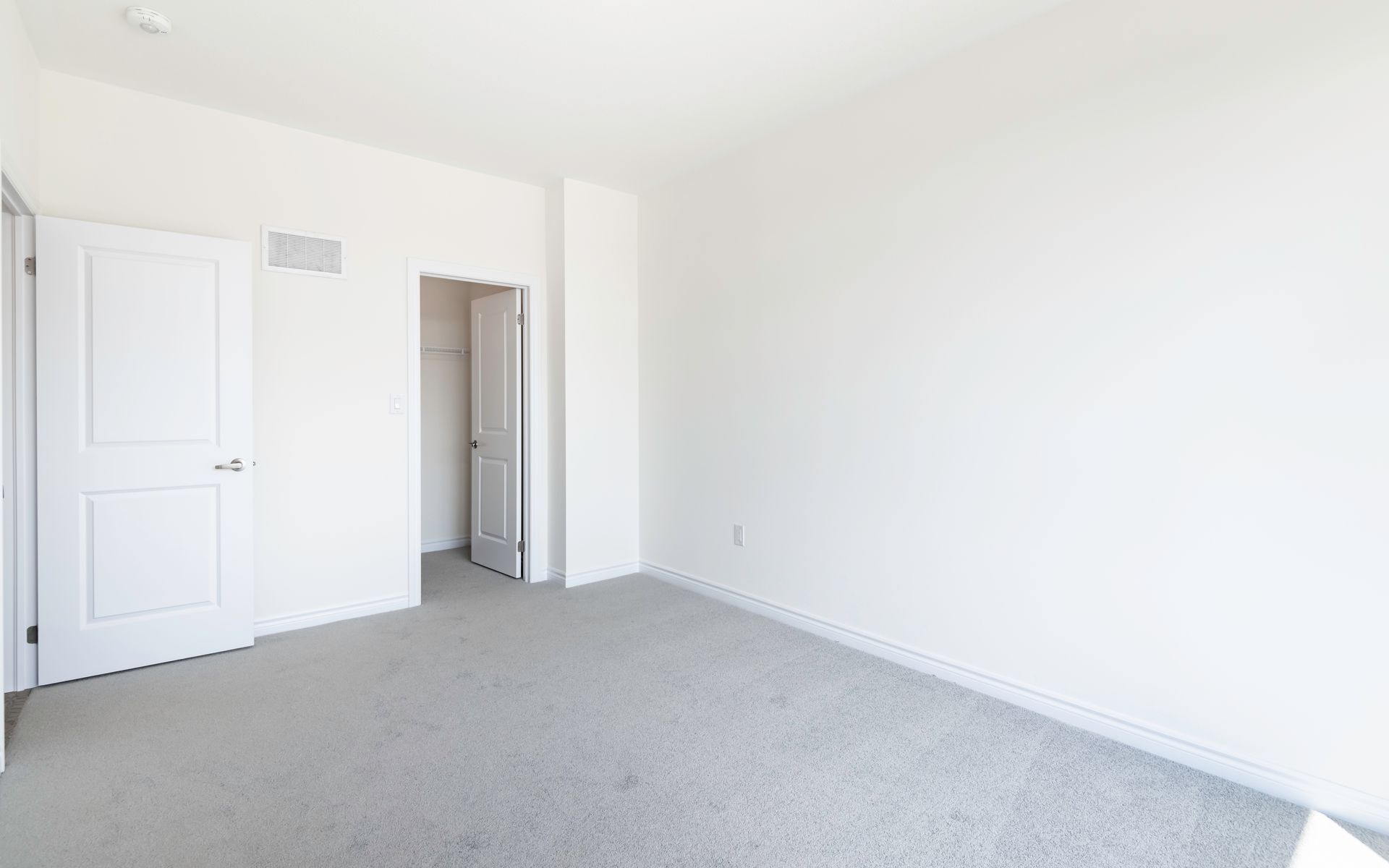 An empty bedroom with a carpeted floor and white walls.