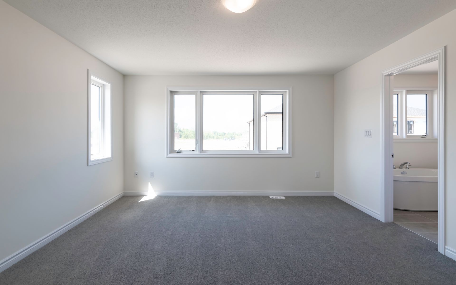 An empty living room with a large window and a gray carpet.