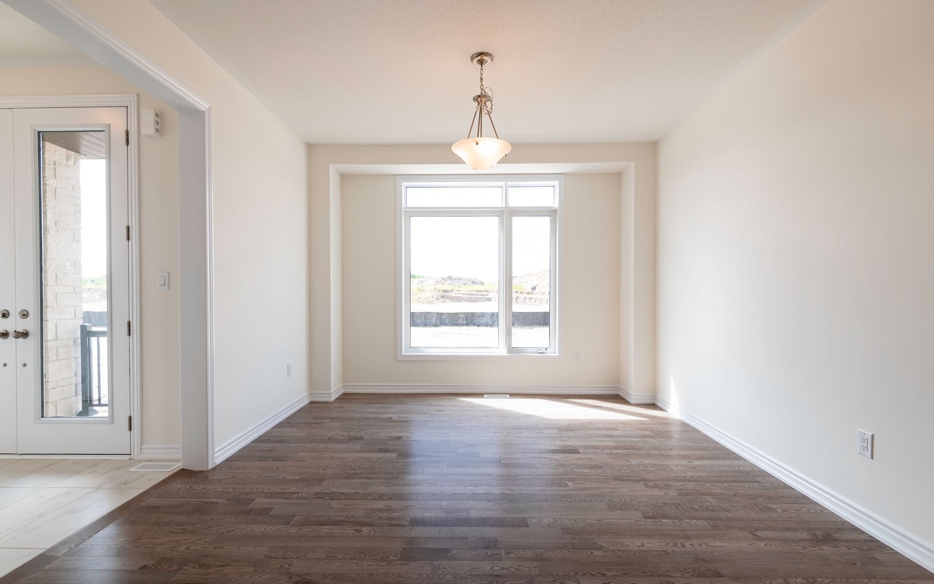 An empty living room with hardwood floors and a large window.