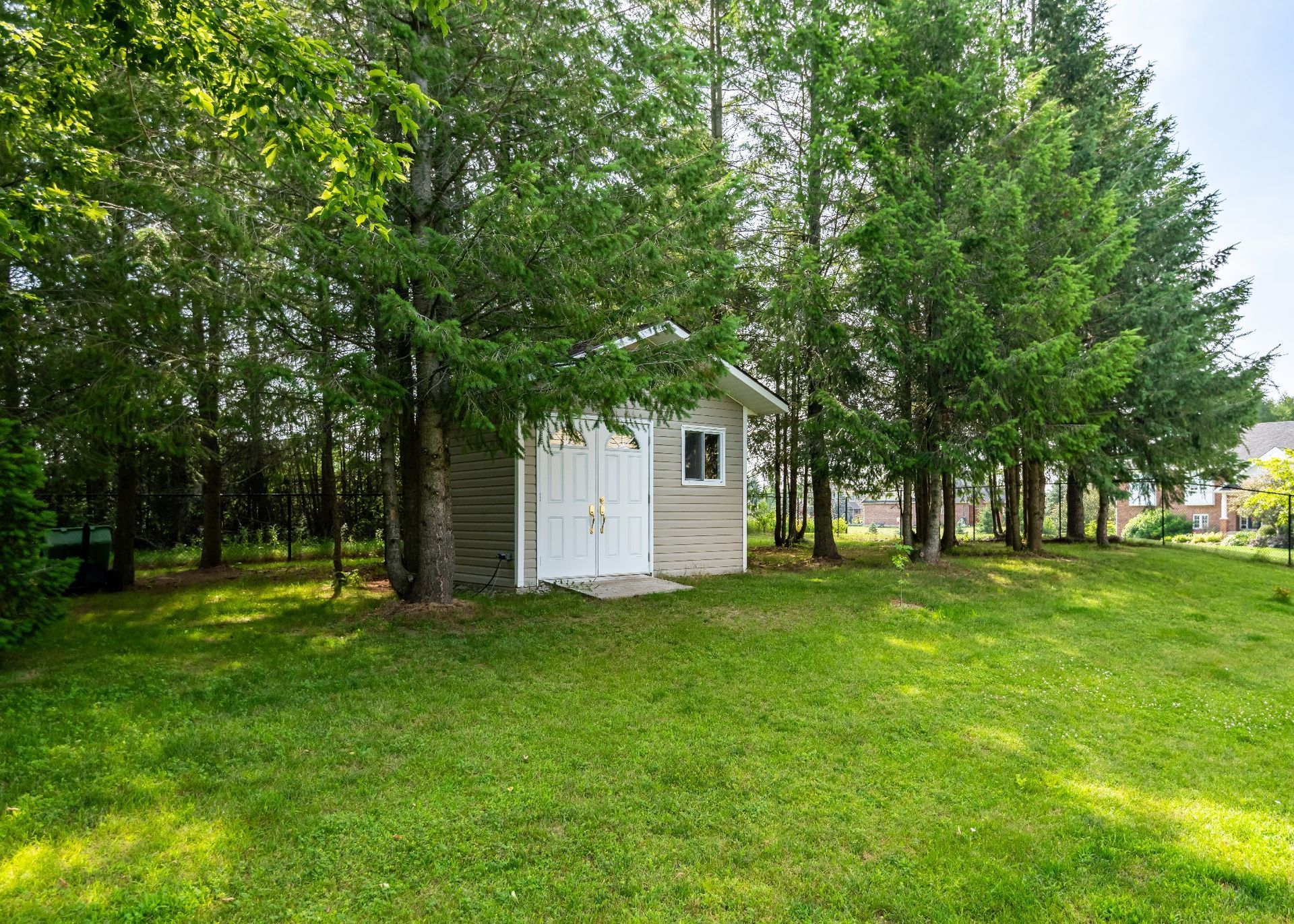 A small white shed is sitting in the middle of a lush green yard surrounded by trees.