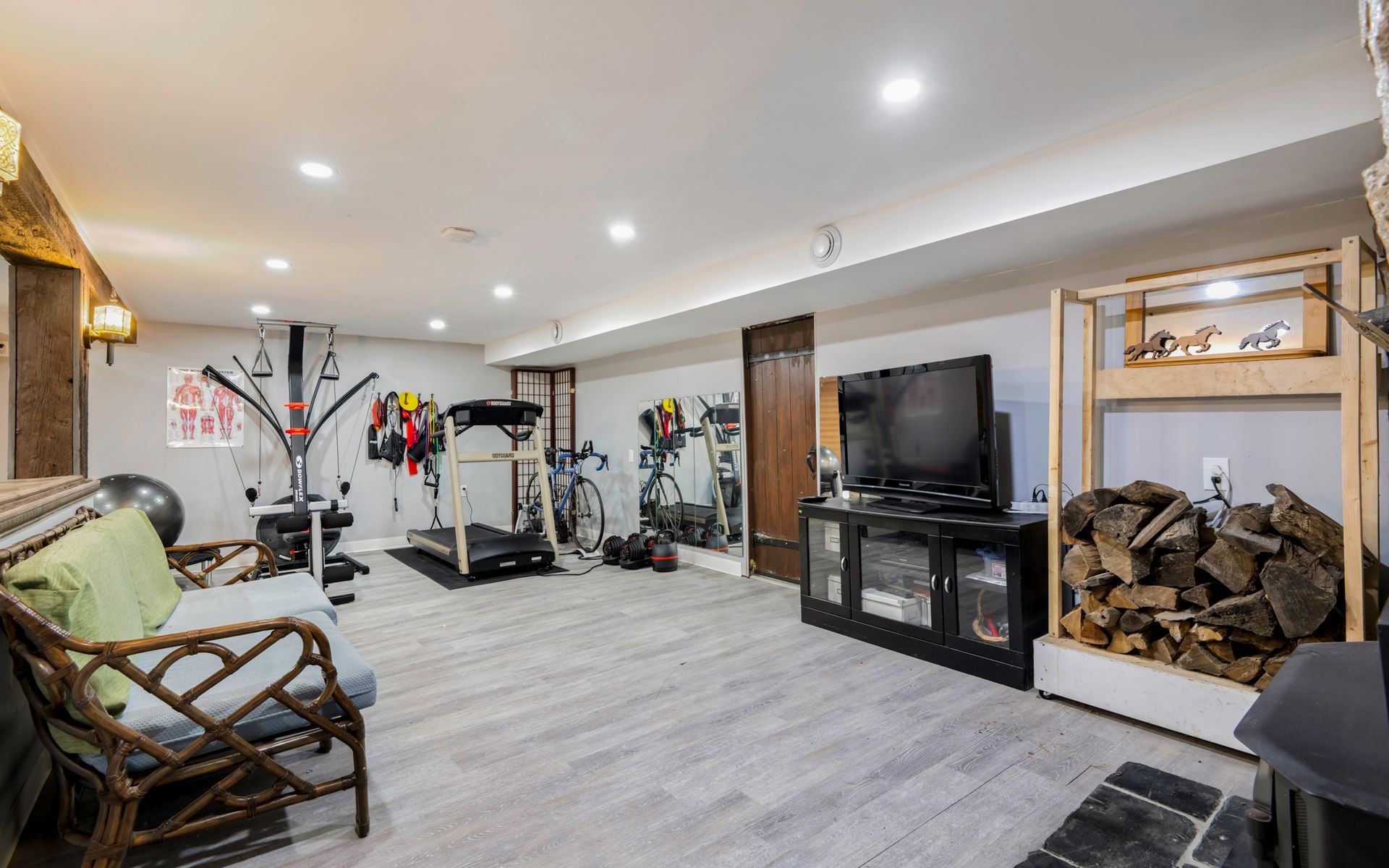 A basement with a treadmill , television , couch and chairs.