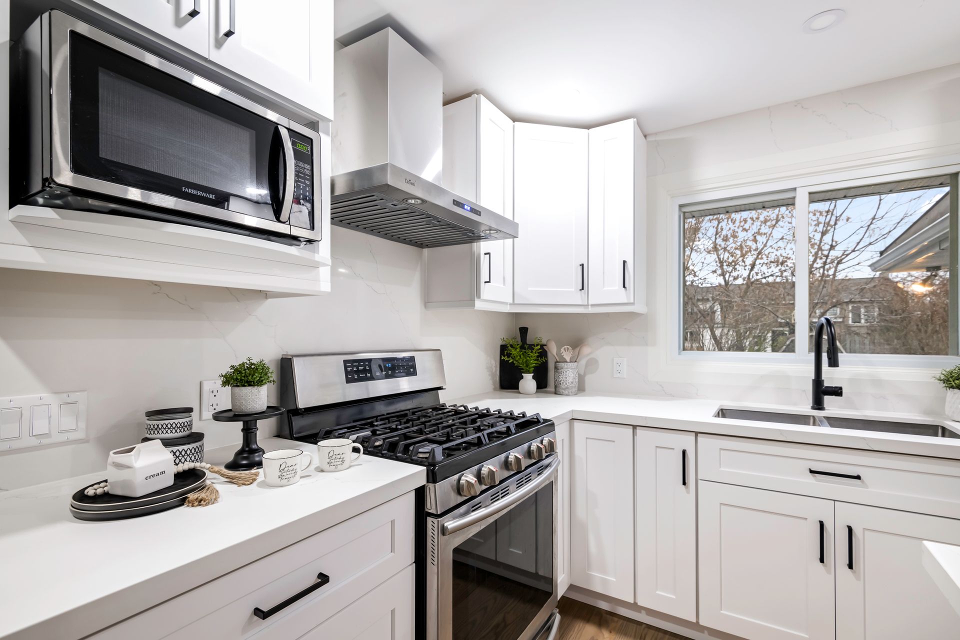 A kitchen with white cabinets , a stove , a microwave , and a sink.