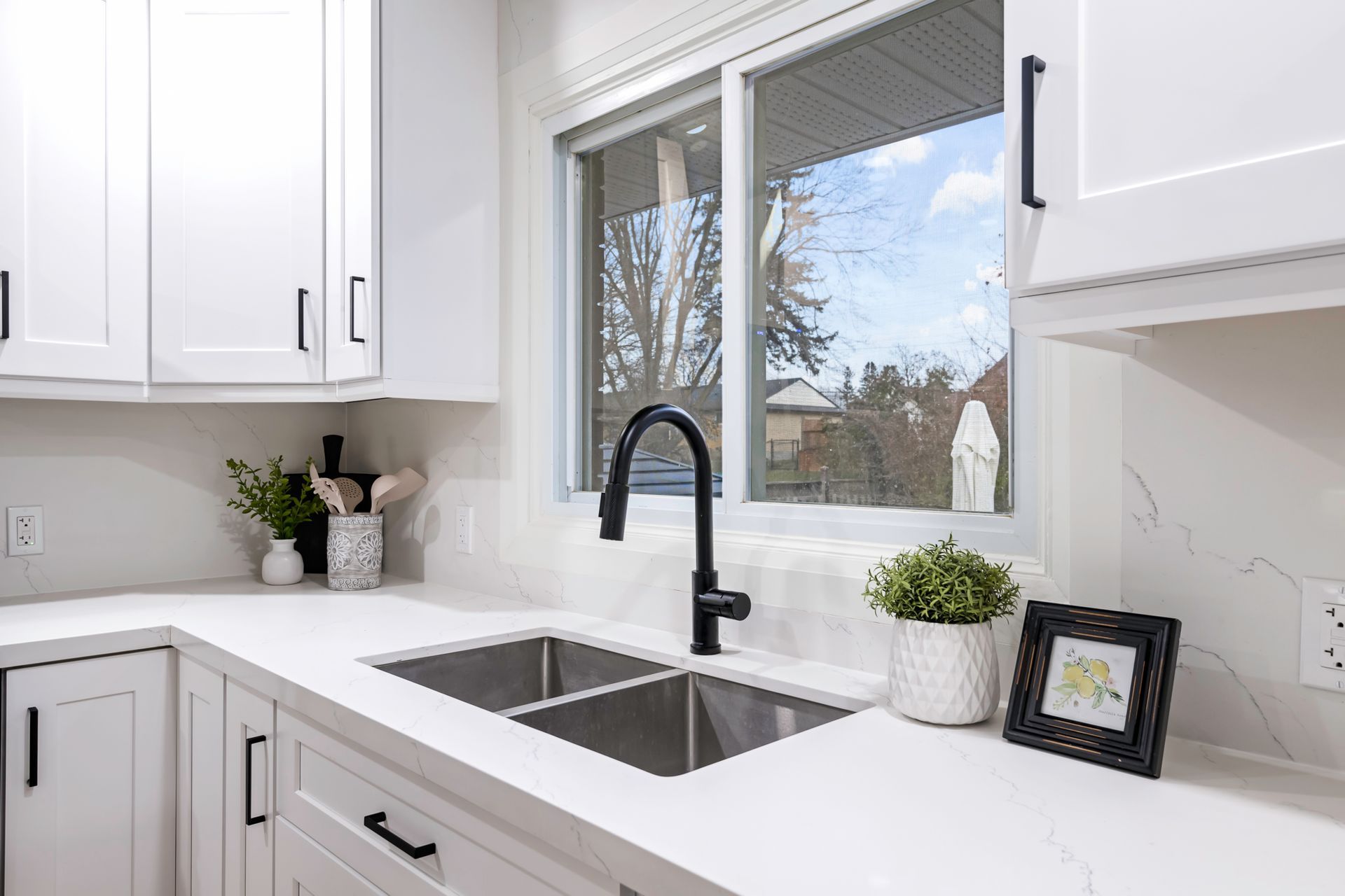 A kitchen with white cabinets , a sink , and a window.