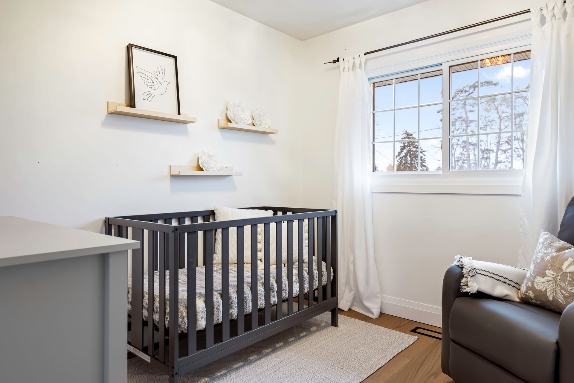 A nursery with a crib , chair , dresser and window.