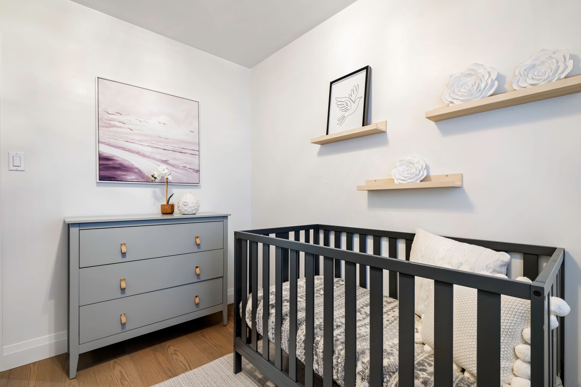 A nursery with a crib , dresser , and painting on the wall.