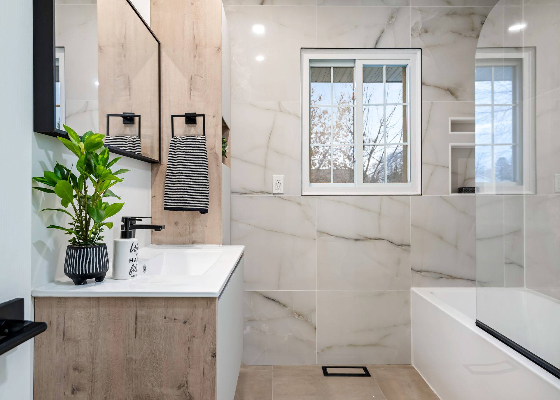 A bathroom with a sink , tub , mirror and window.