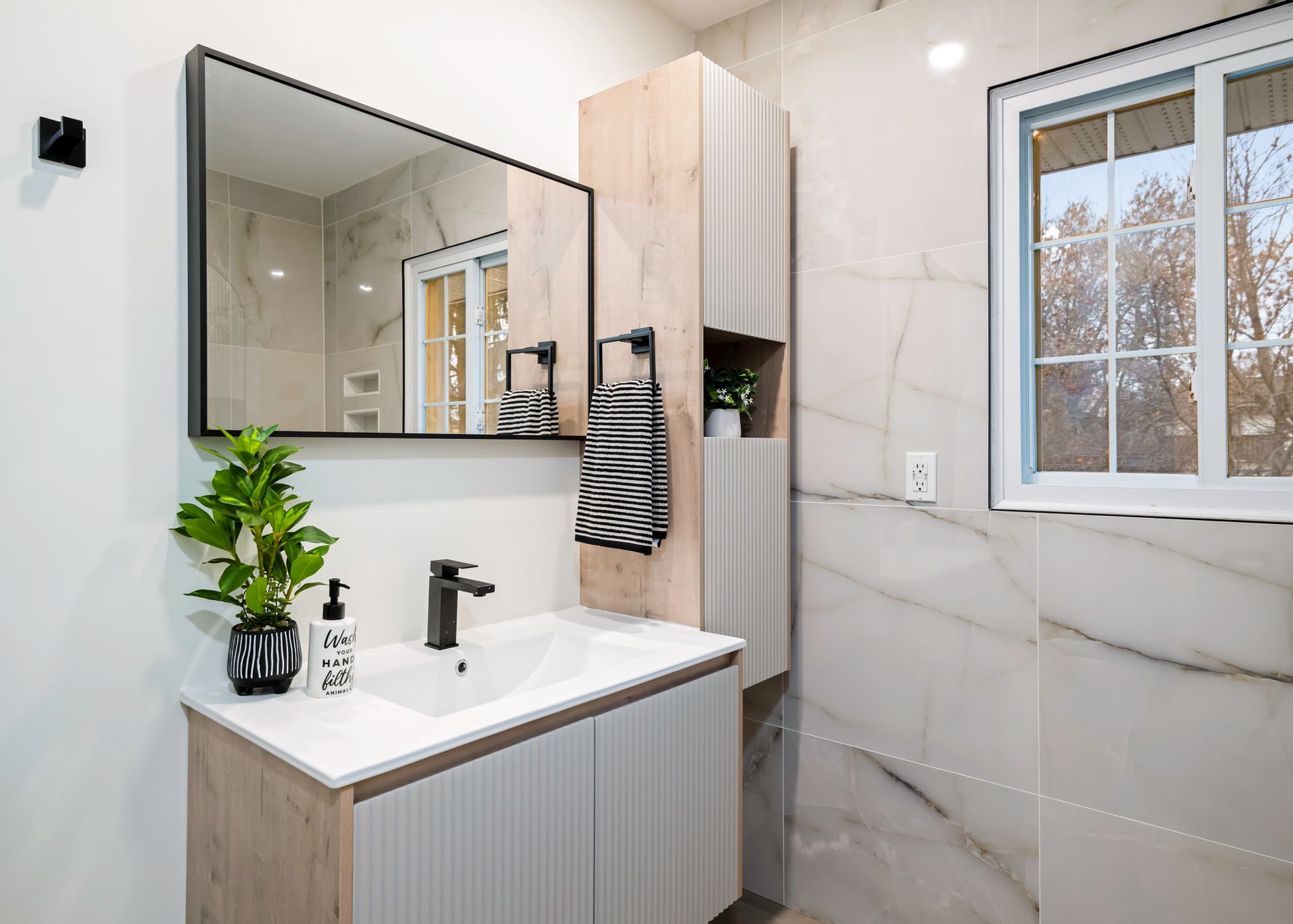 A bathroom with a sink , mirror and window.