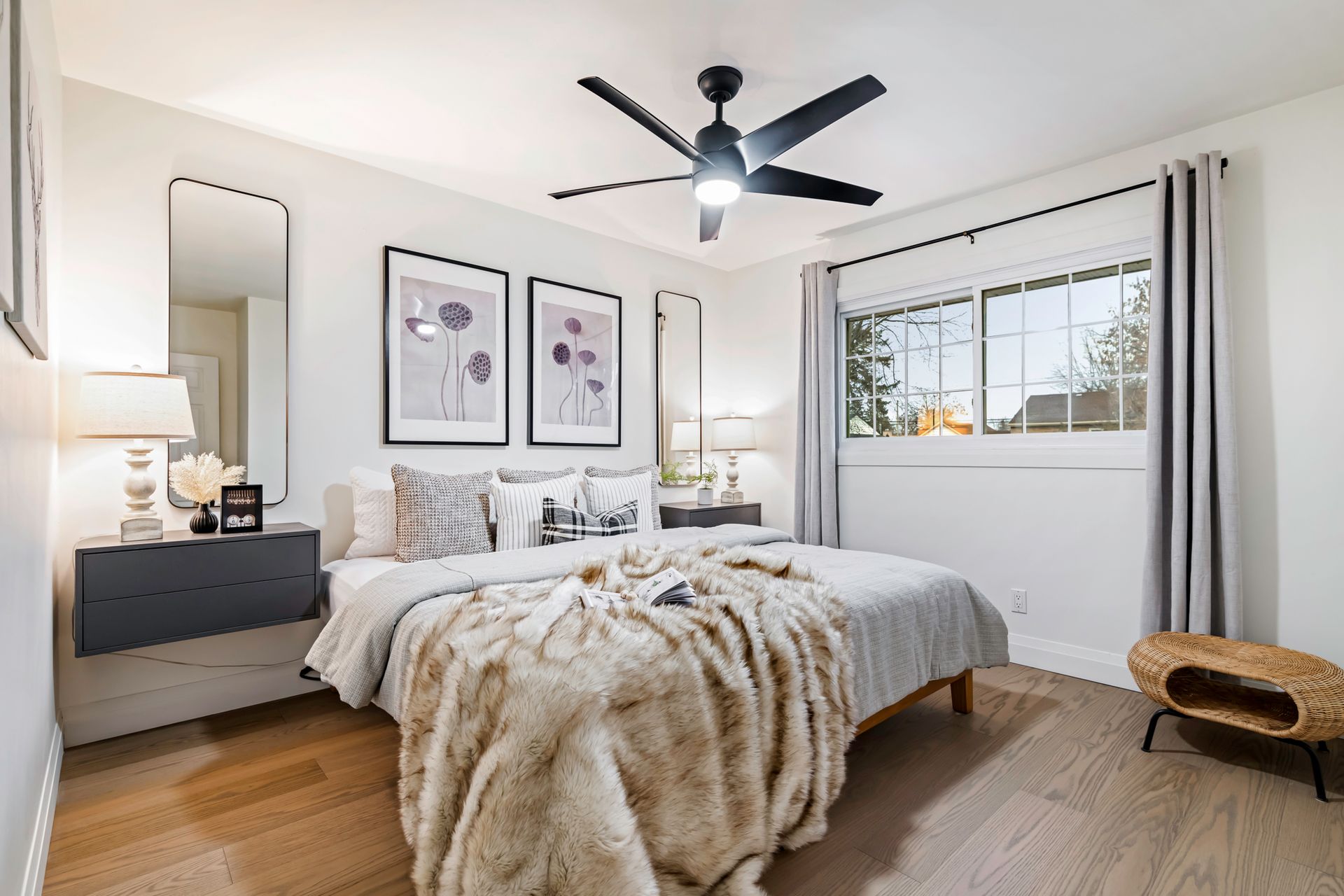 A bedroom with a bed , two mirrors , a ceiling fan and a window.