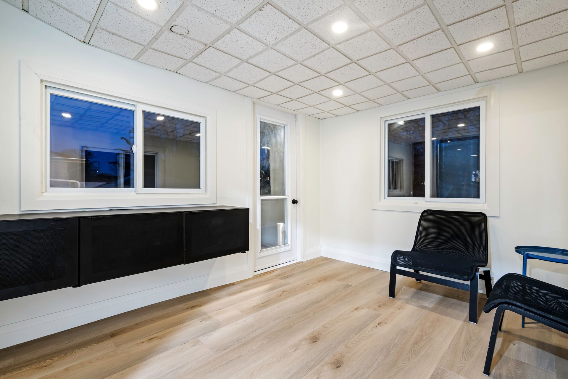 A room with a wooden floor , two chairs and two windows.