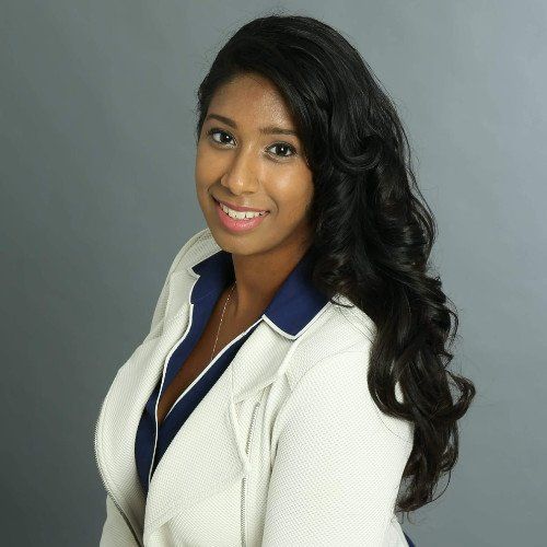 A woman wearing a white jacket and a blue shirt smiles for the camera