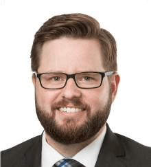 A man with a beard and glasses is wearing a suit and tie.
