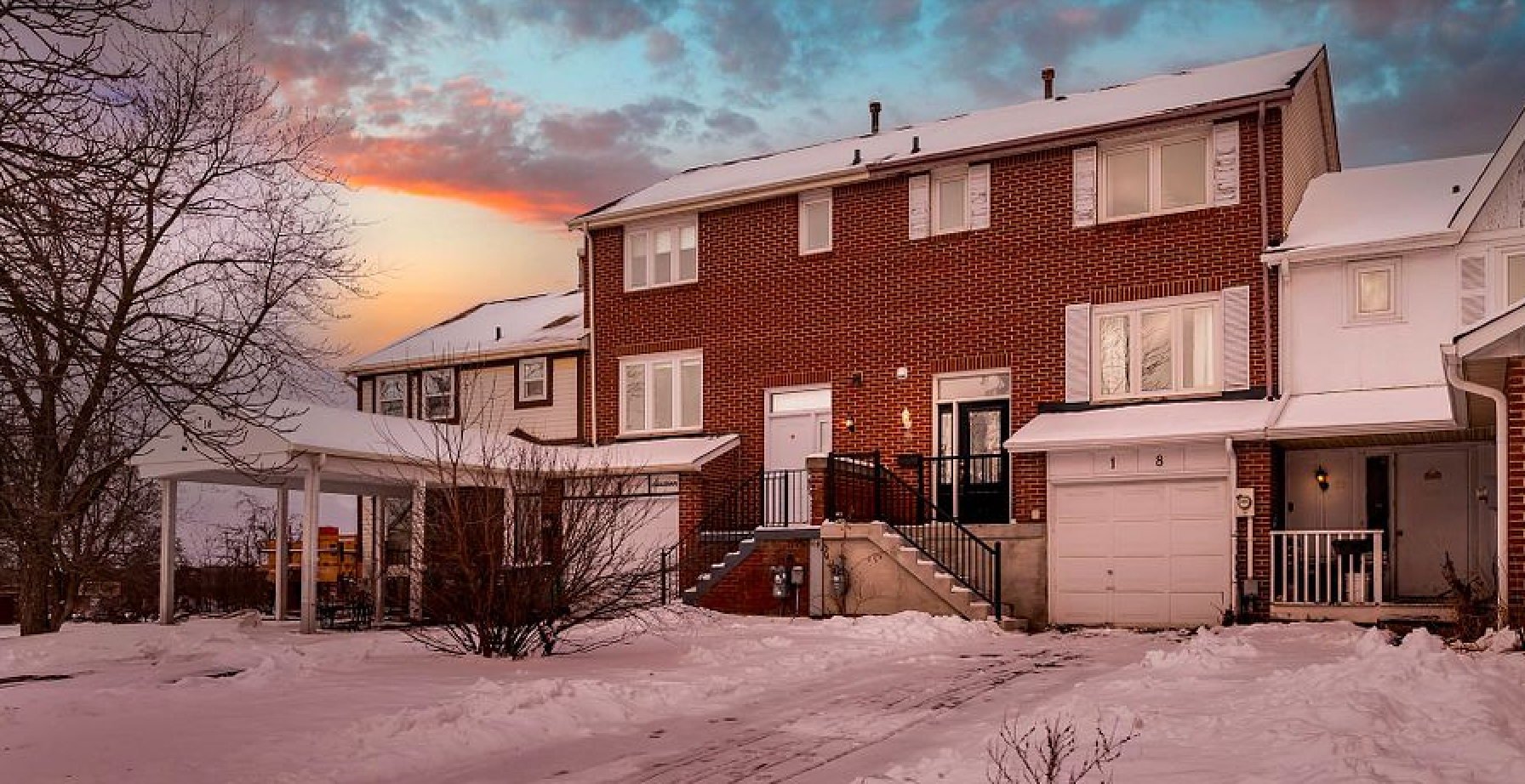 A brick house with a garage and a porch is covered in snow.