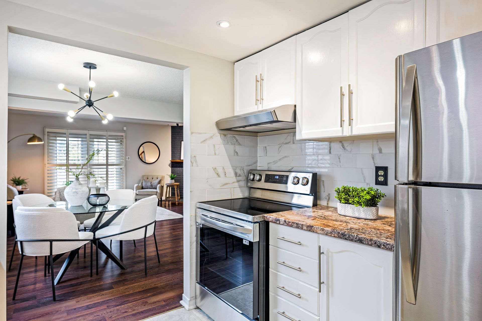 A kitchen with white cabinets , a stove , a refrigerator , and a dining room.