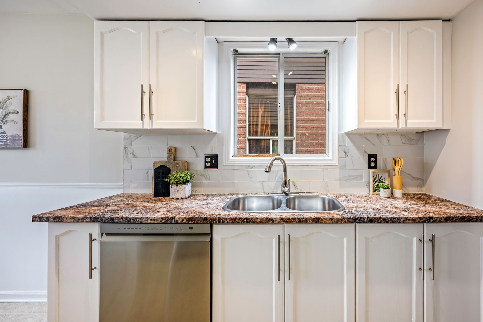 A kitchen with white cabinets , a sink , a dishwasher , and a window.
