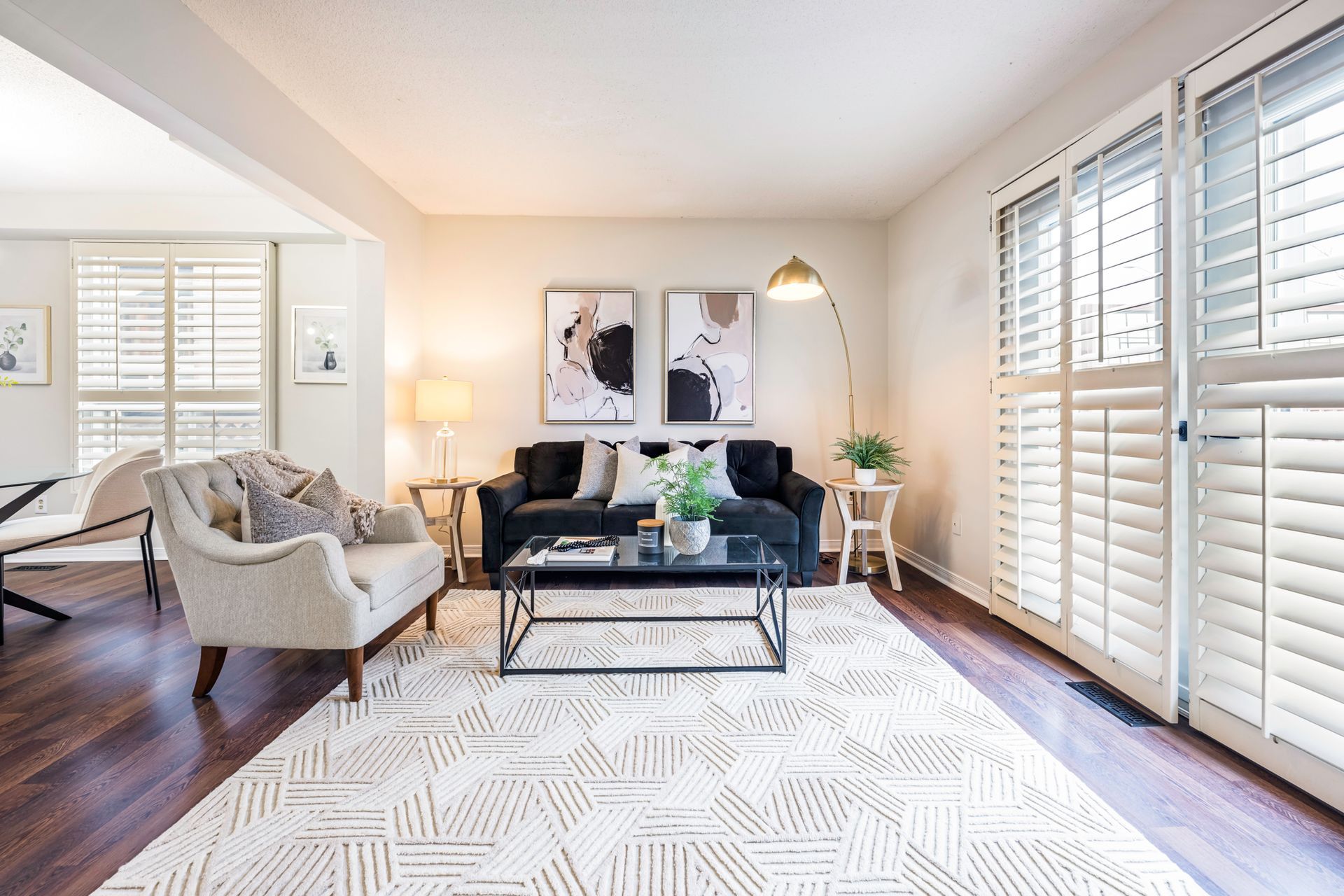 A living room with a couch , chair , coffee table and shutters.